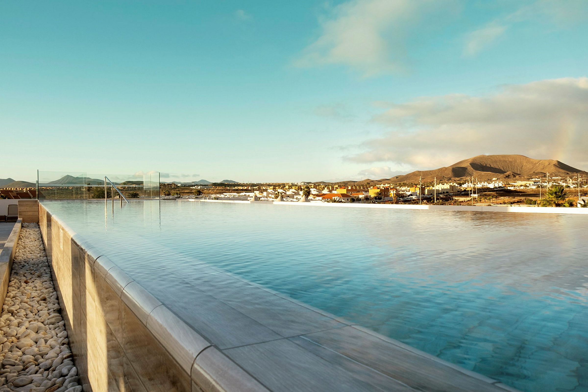 En infinitypool under en klar himmel med udsigt over en by og bjerge i baggrunden. (AI-genereret tekst)