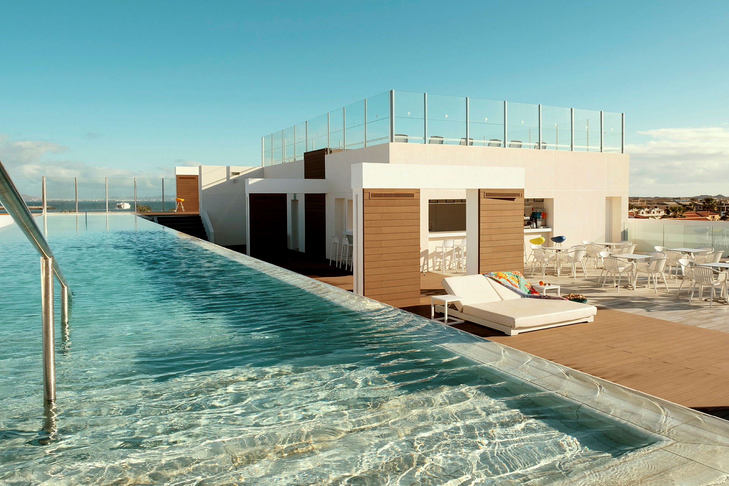 En tagterrasse med en lang infinitypool, liggestole og lounge møbler under åben himmel. (AI-genereret tekst)