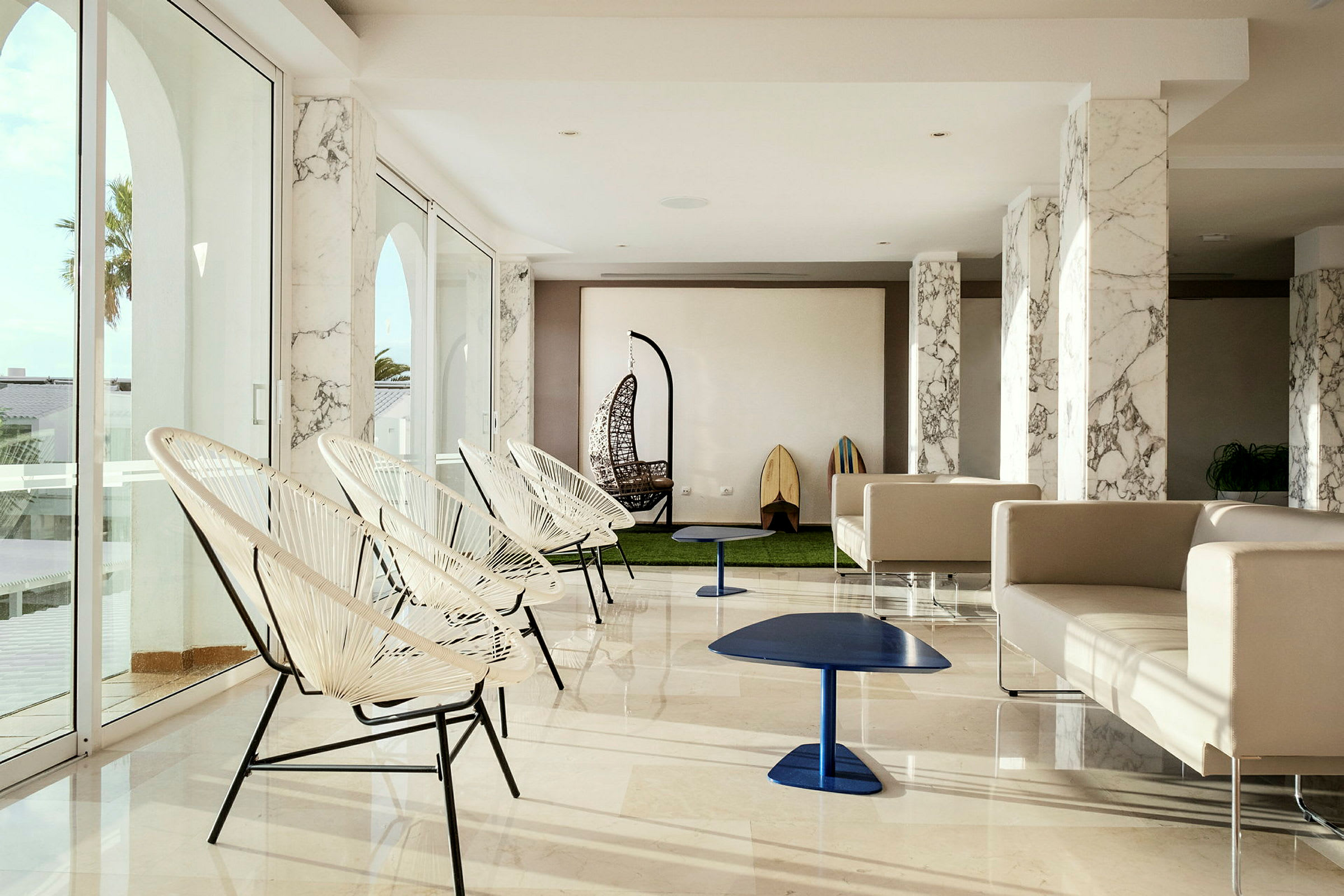Et moderne og lyst rum med store glasvinduer, elegante stole, sofagrupper og dekorative detaljer. (AI-genereret tekst)