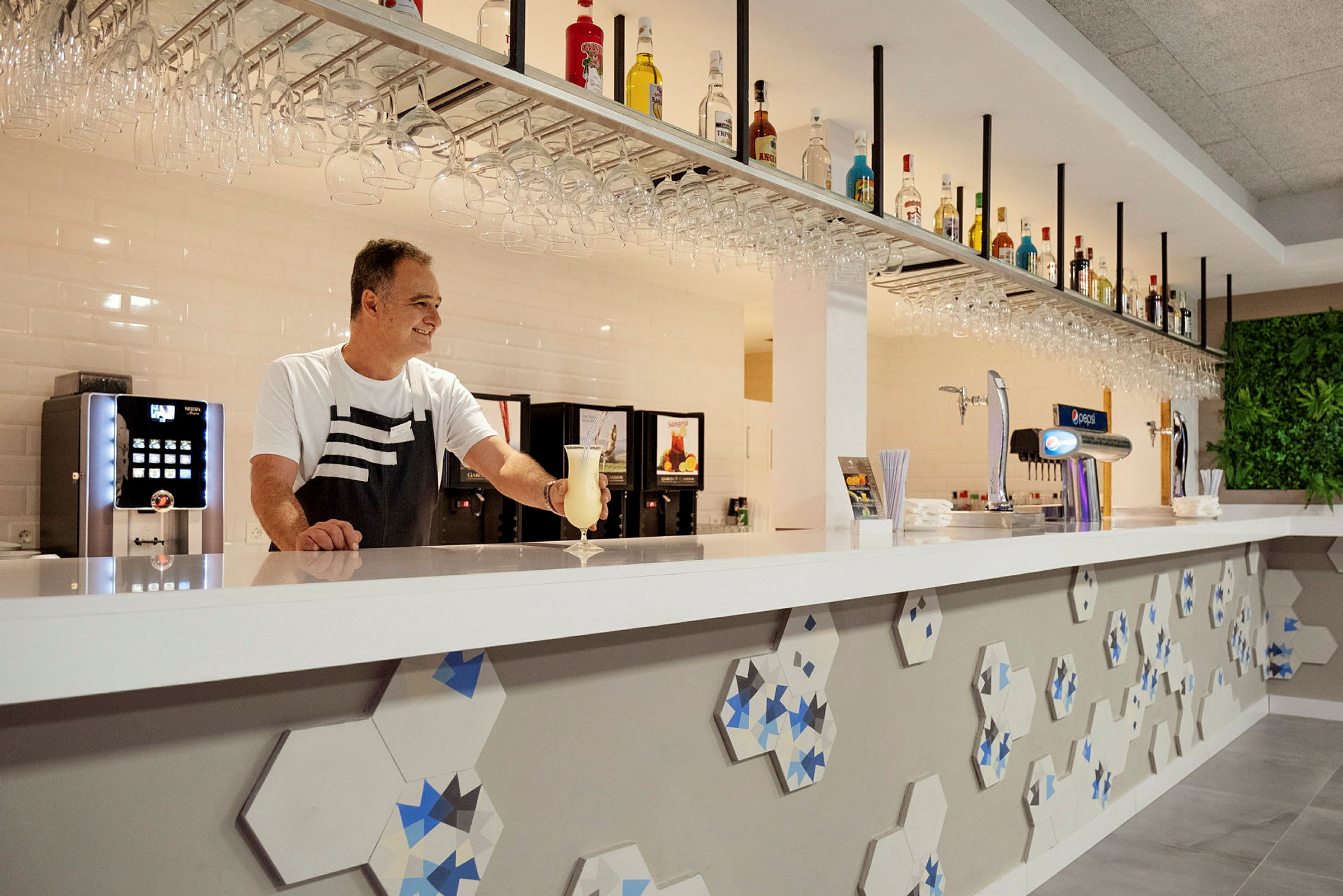 En bartender ved en moderne bardisk med flasker og glas hængende ovenfor. (AI-genereret tekst)