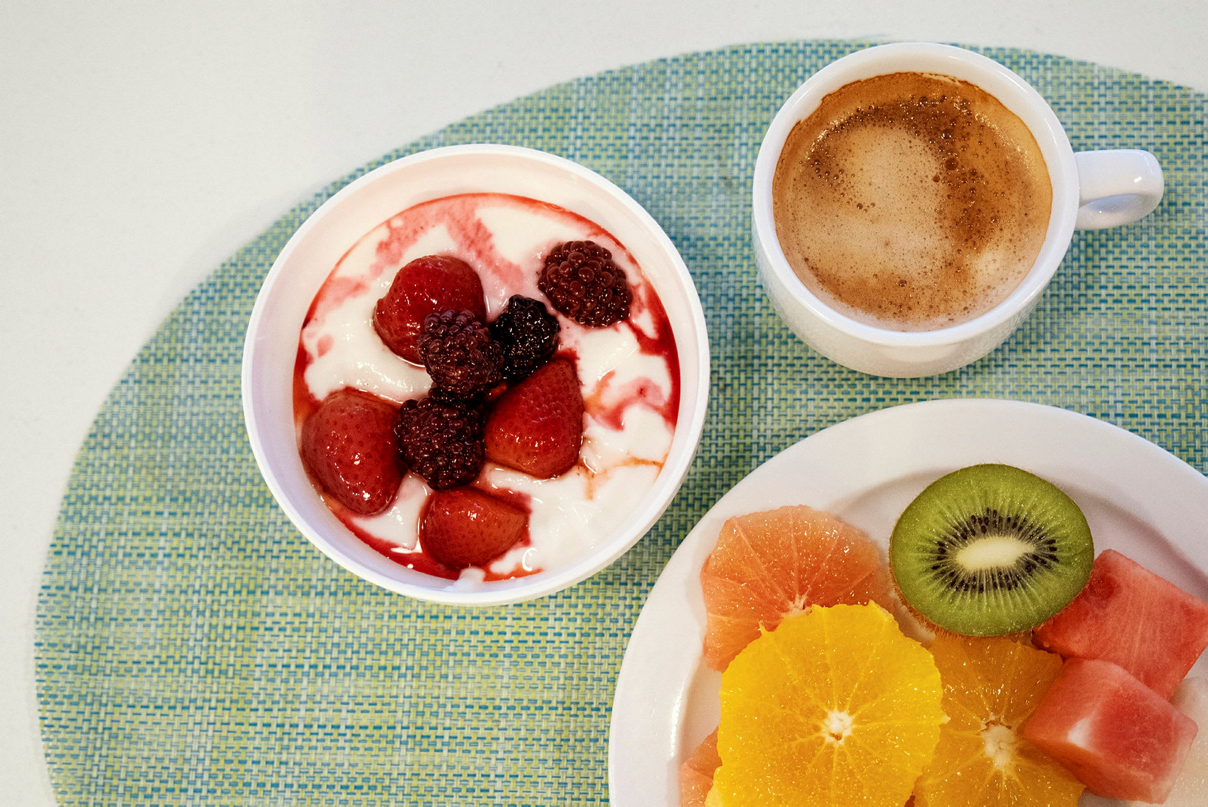En morgenmad med yoghurt toppet med bær, en kop kaffe og skåret frisk frugt. (AI-genereret tekst)