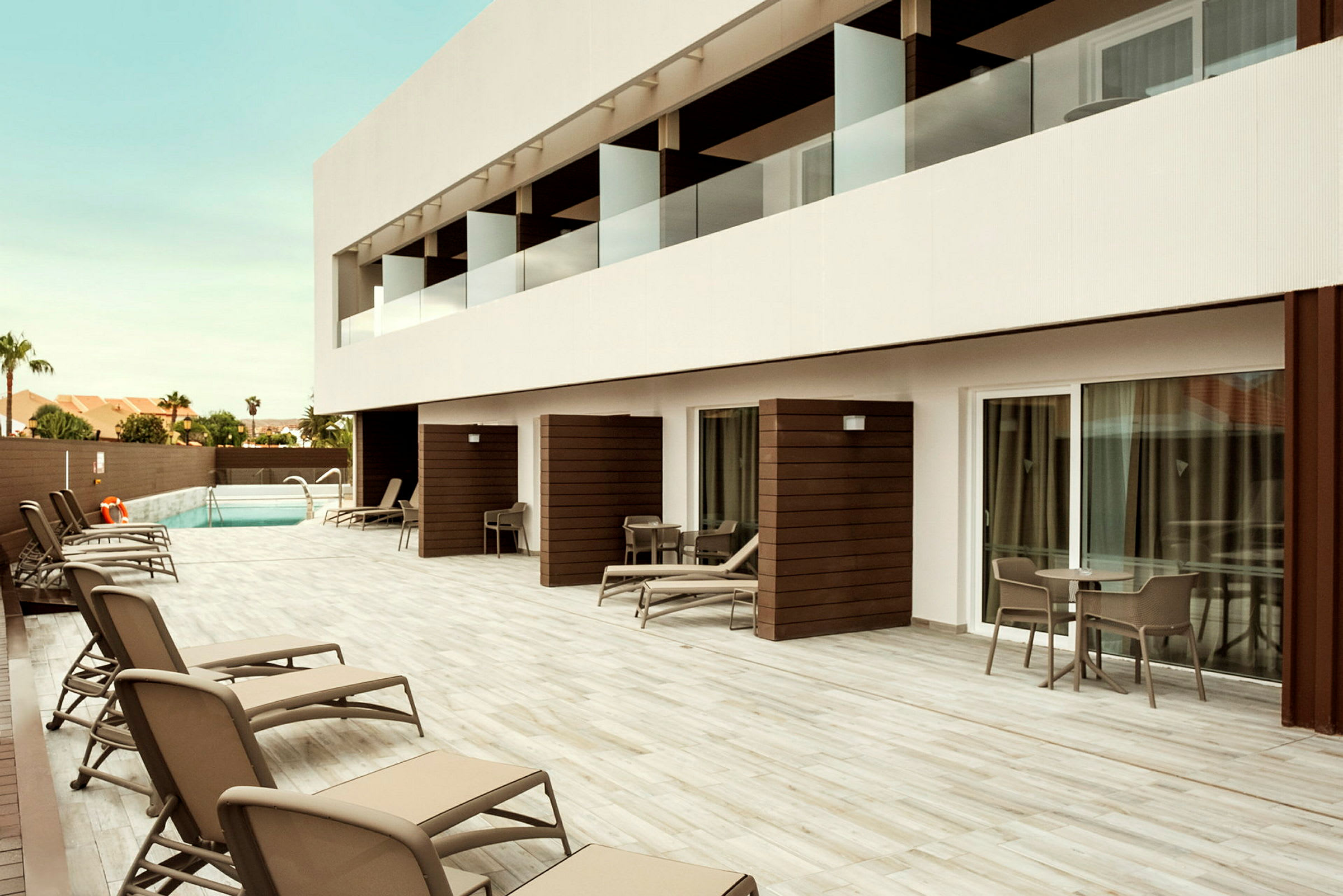 Hotelområde med terrasseområde, liggestole og en pool i baggrunden. (AI-genereret tekst)