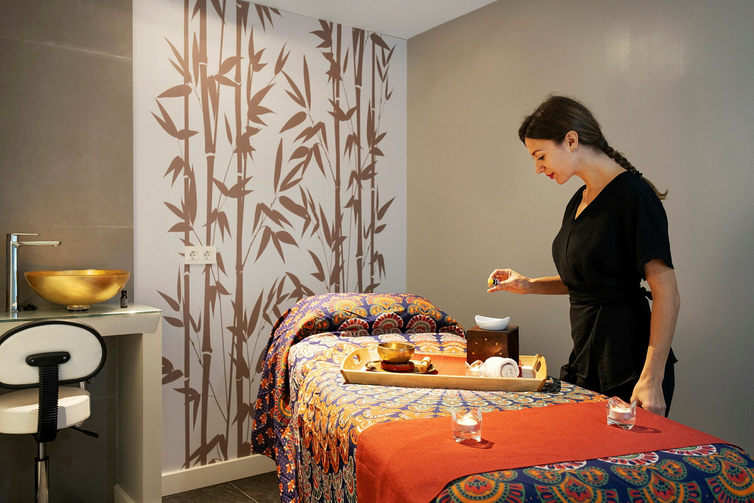 Et spa- eller massagerum med en dekoreret massagebænk, en bakke med tilbehør og en person ved siden af. (AI-genereret tekst)