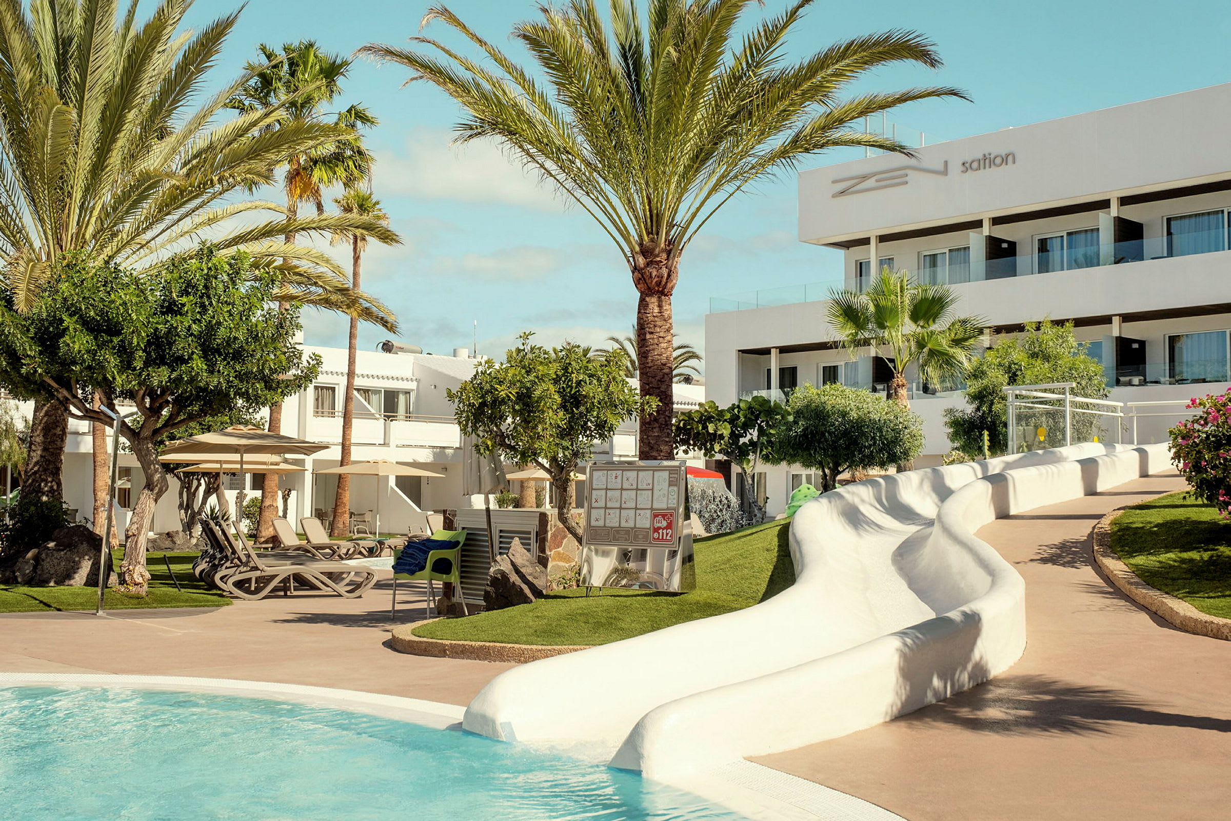 Hotellets poolområde med grønne omgivelser, liggestole og en vandrutsjebane. (AI-genereret tekst)