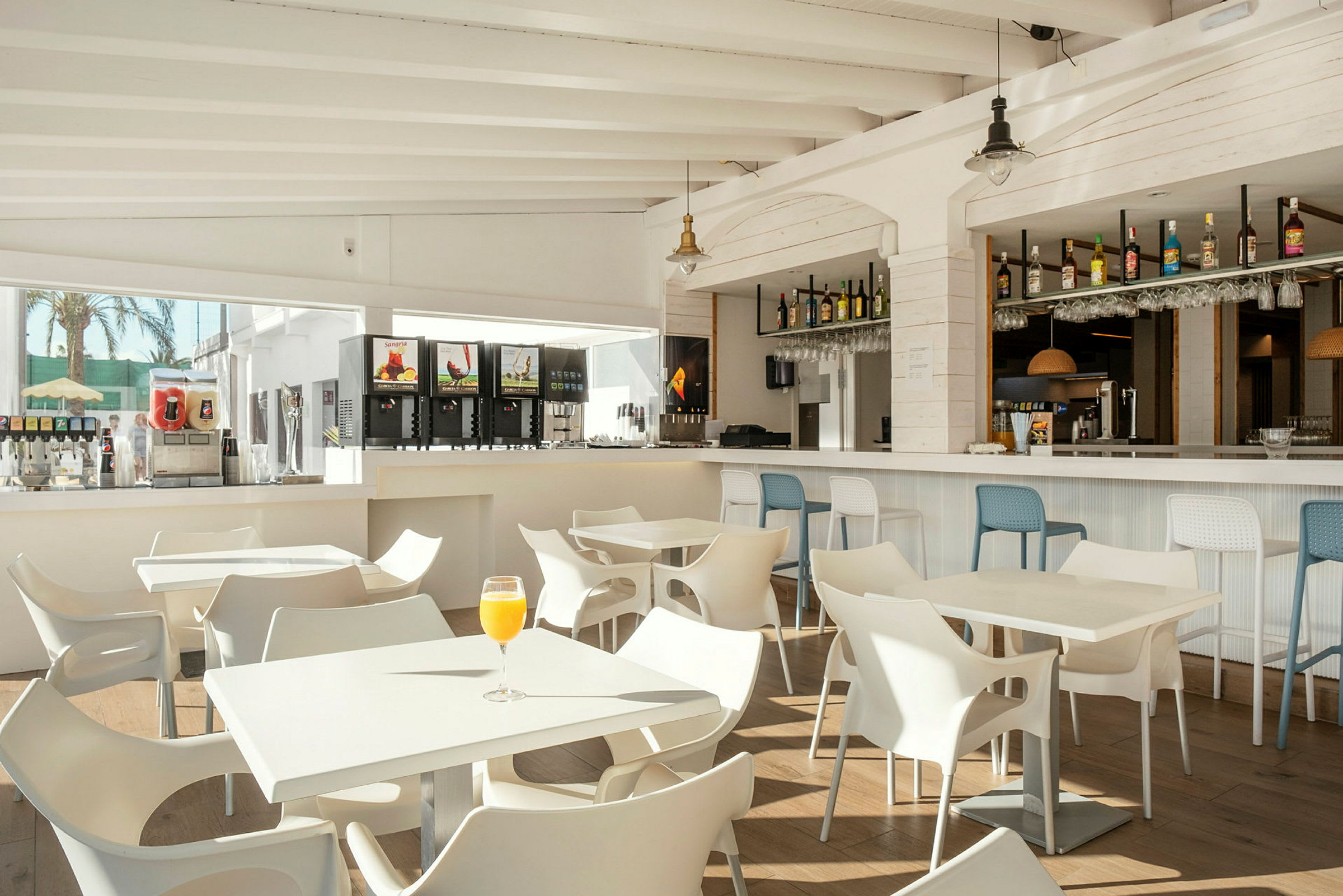 Et lyst og moderne indrettet caféområde med hvide borde og stole samt en bardisk i baggrunden. (AI-genereret tekst)