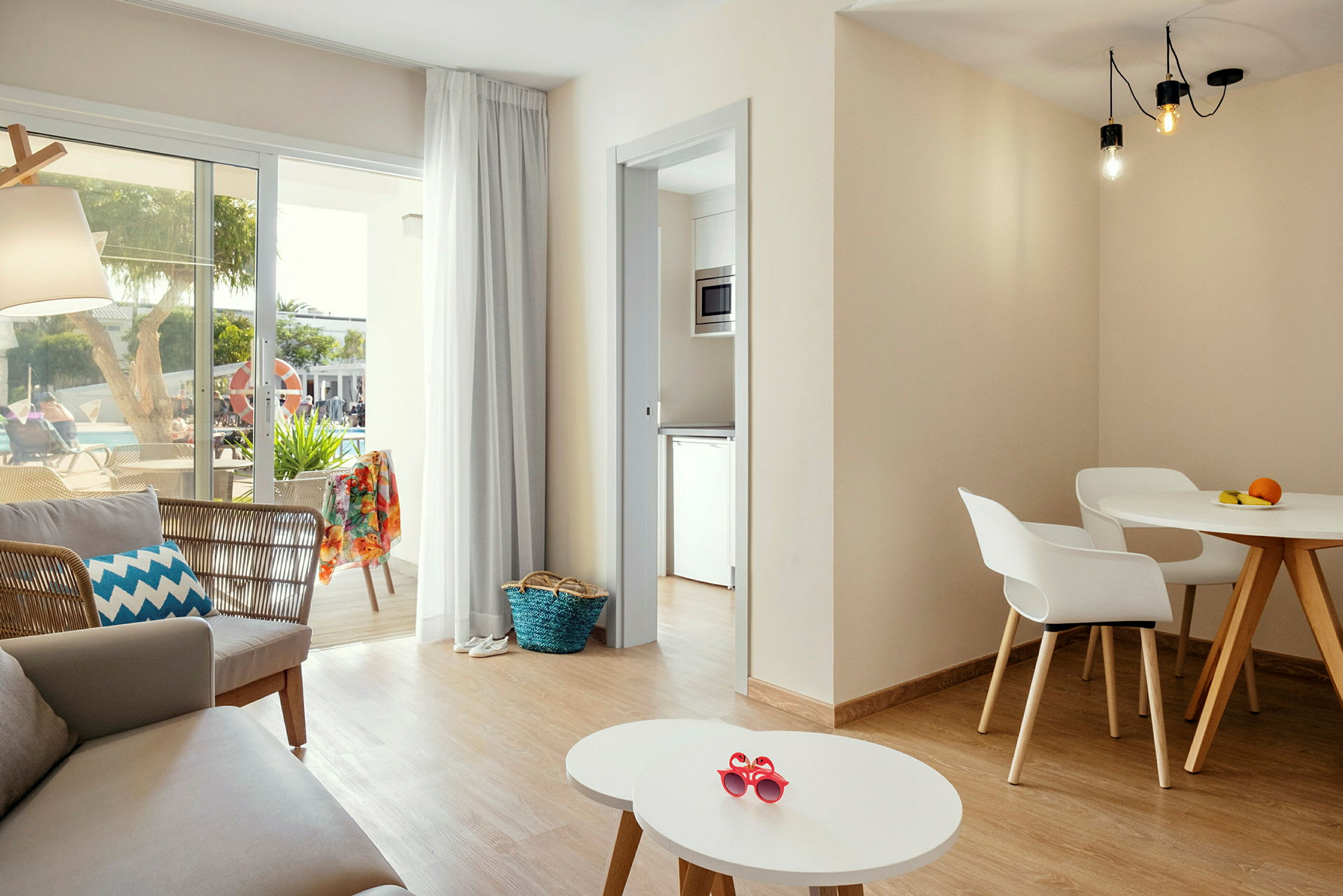 En lys og moderne indrettet stue med siddeområde, spisebord og store vinduer, der vender ud mod en terrasse med udsigt over en pool. (AI-genereret tekst)