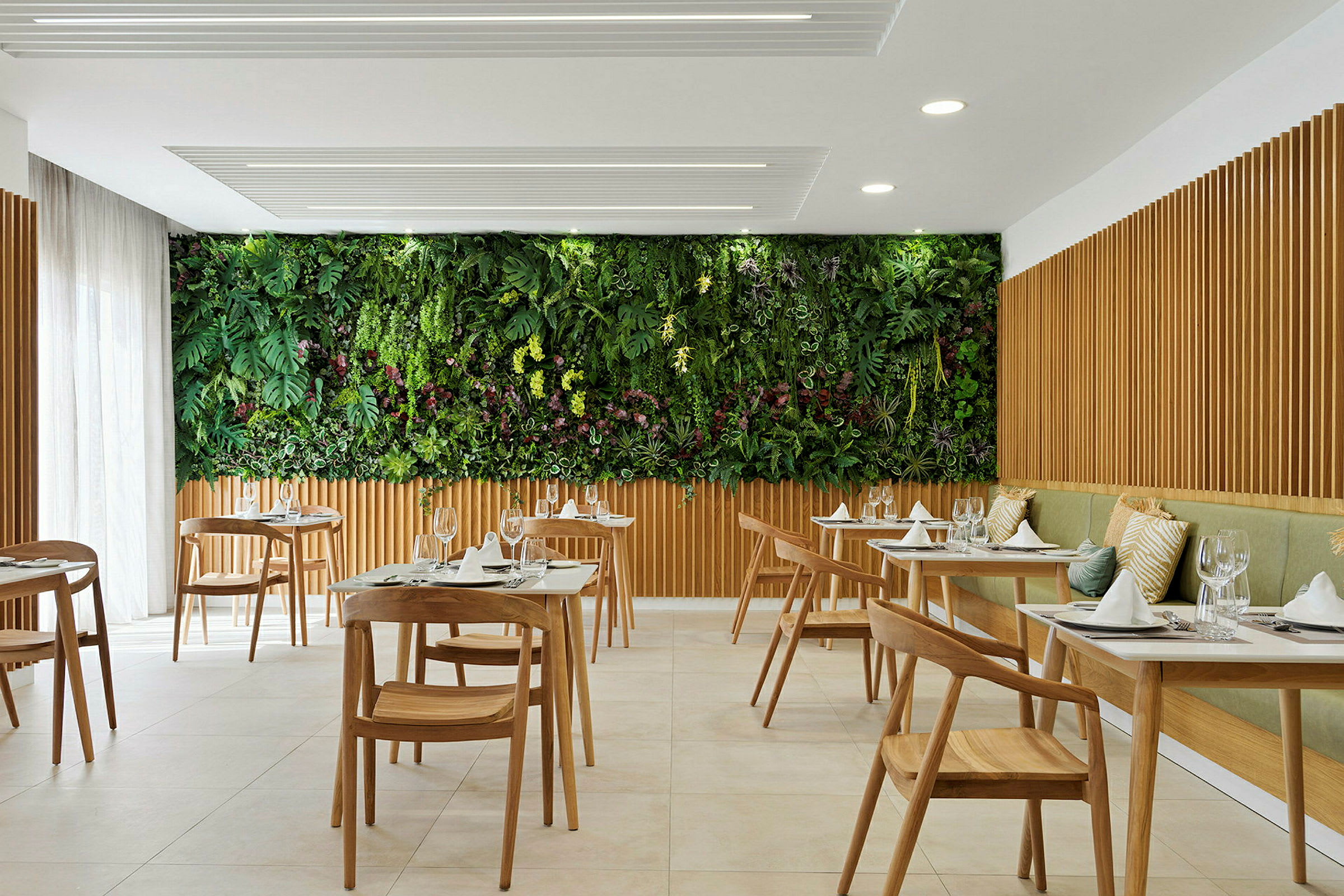 En moderne restaurant med træborde og -stole samt en grøn væg med planter. (AI-genereret tekst)