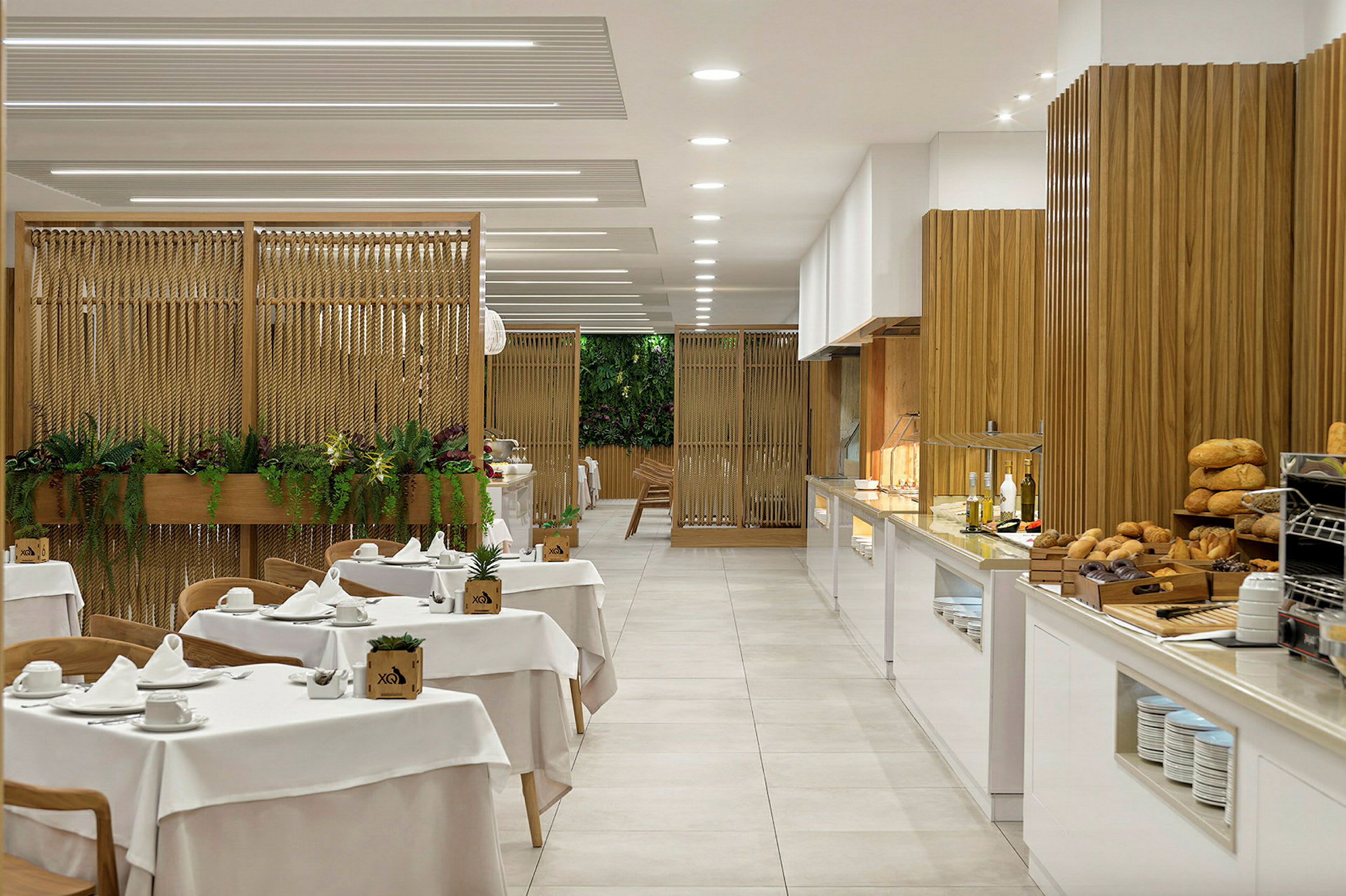 Restaurant med dækkede borde og en buffet med brød og olier samt en dekorativ væg med planter. (AI-genereret tekst)
