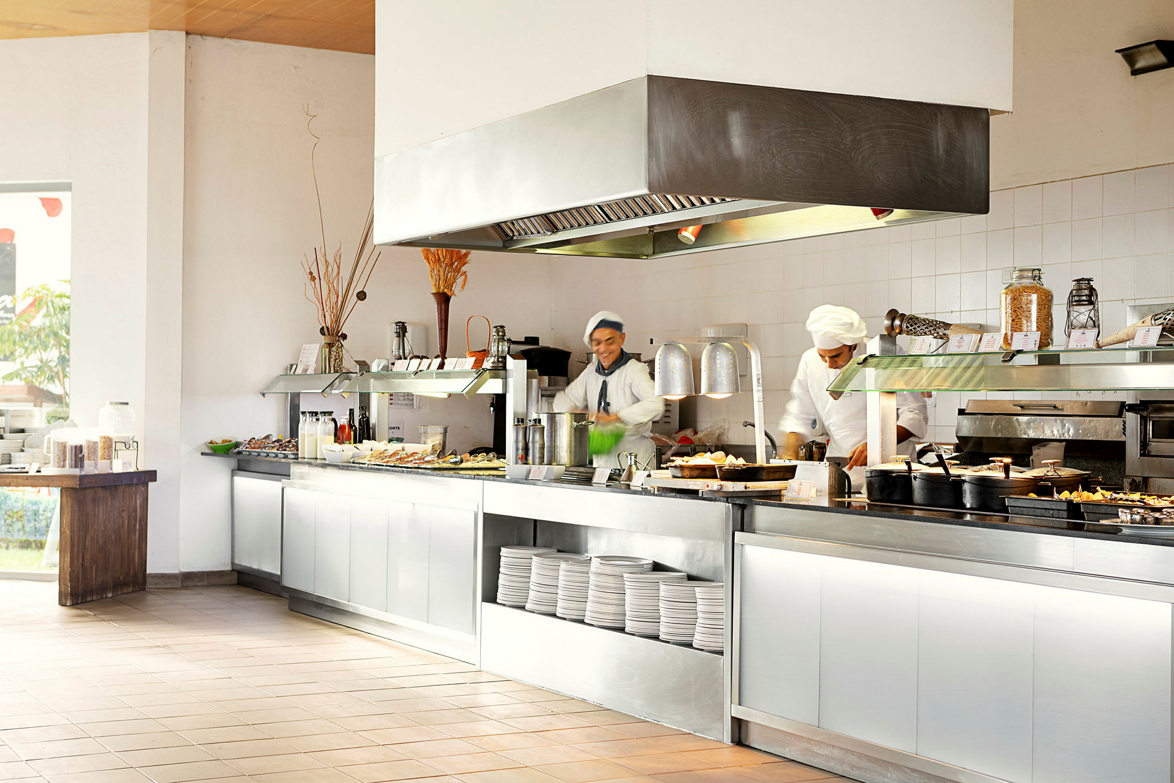 En restaurantbuffet med forskellige retter og tallerkener placeret på et serveringsbord. Kokke forbereder mad. (AI-genereret tekst)