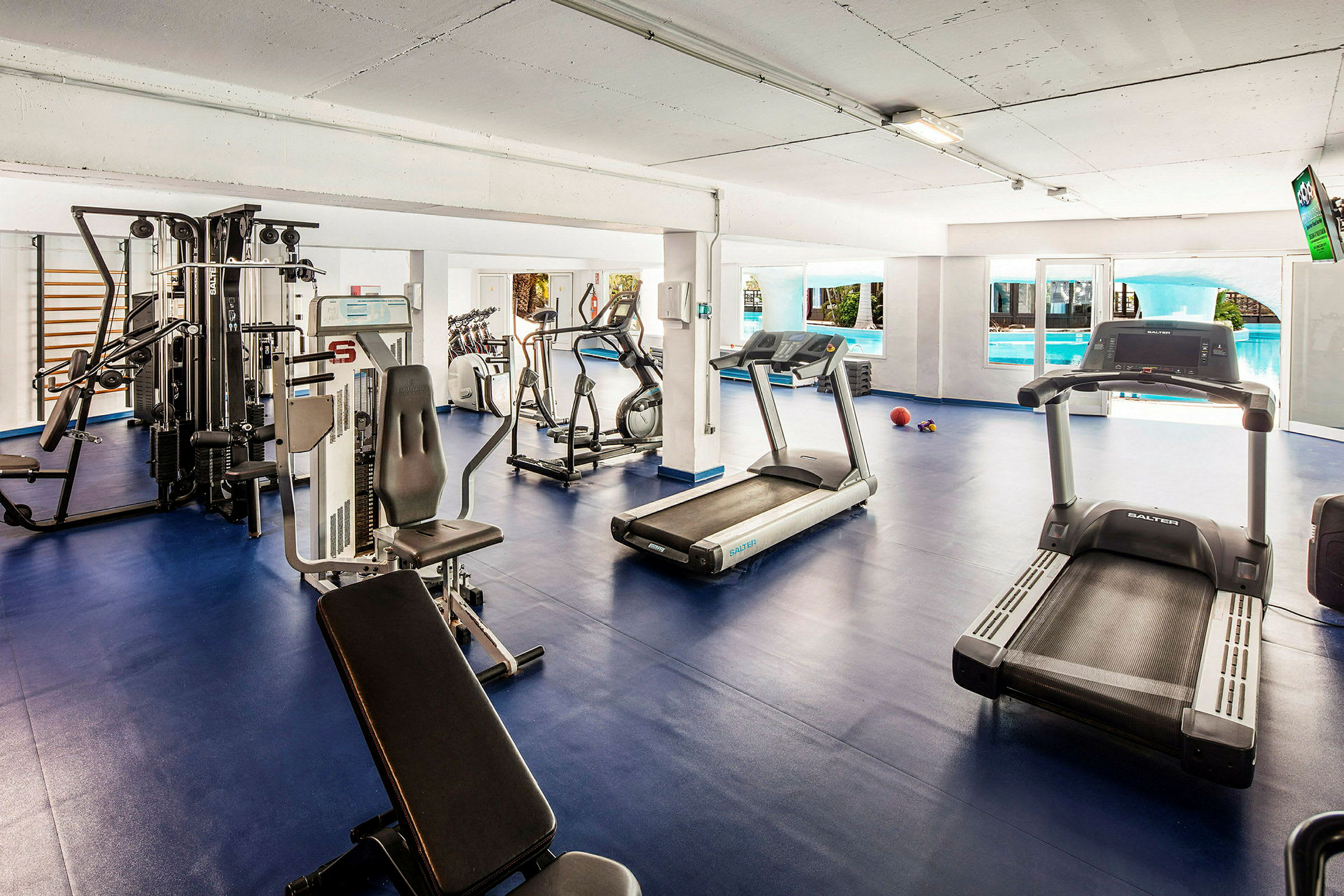 Fitnessrum med træningsmaskiner og løbebånd, blåt gulv. (AI-genereret tekst)