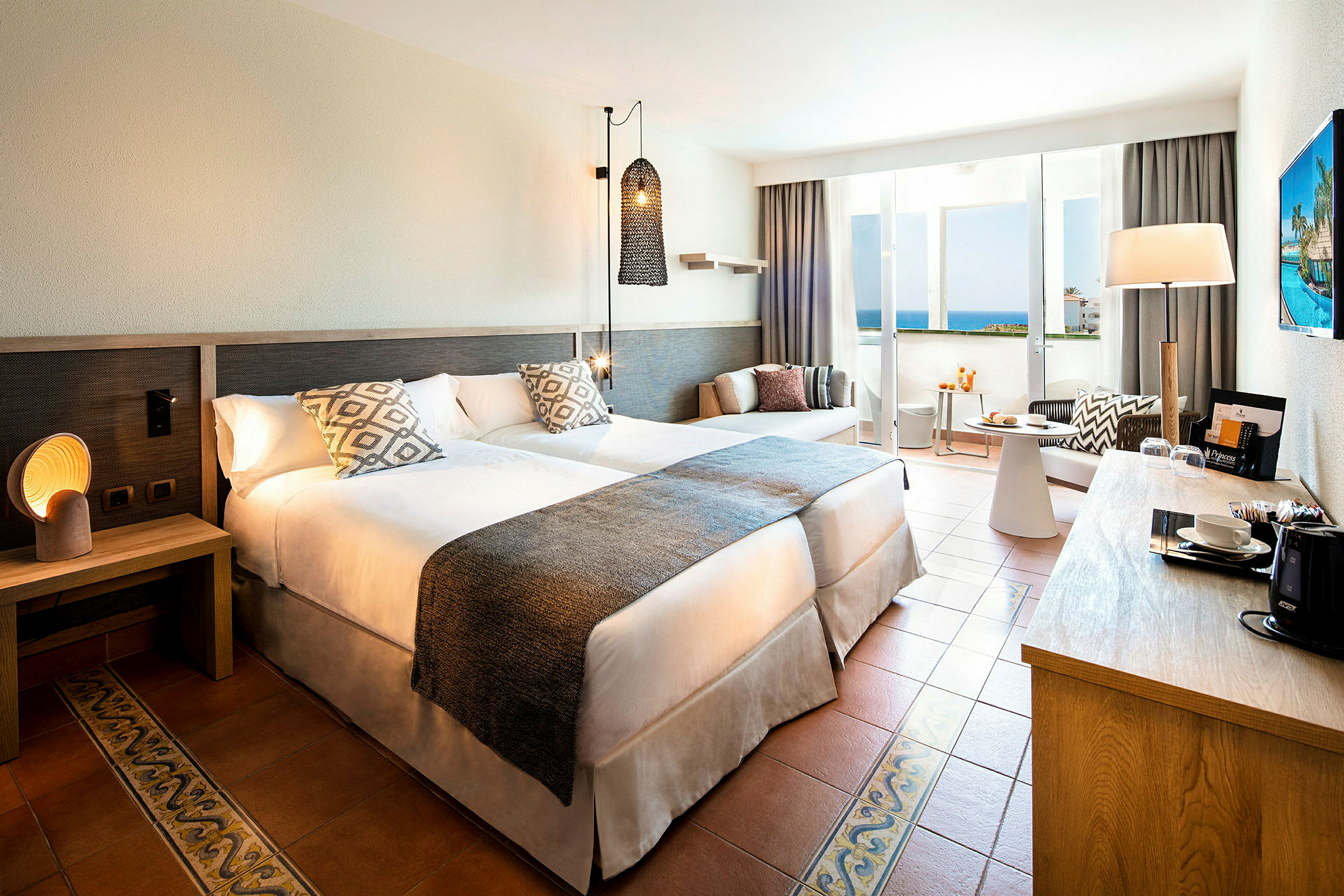 Hotelværelse med to senge, natbord, siddeområde og altan med havudsigt. (AI-genereret tekst)