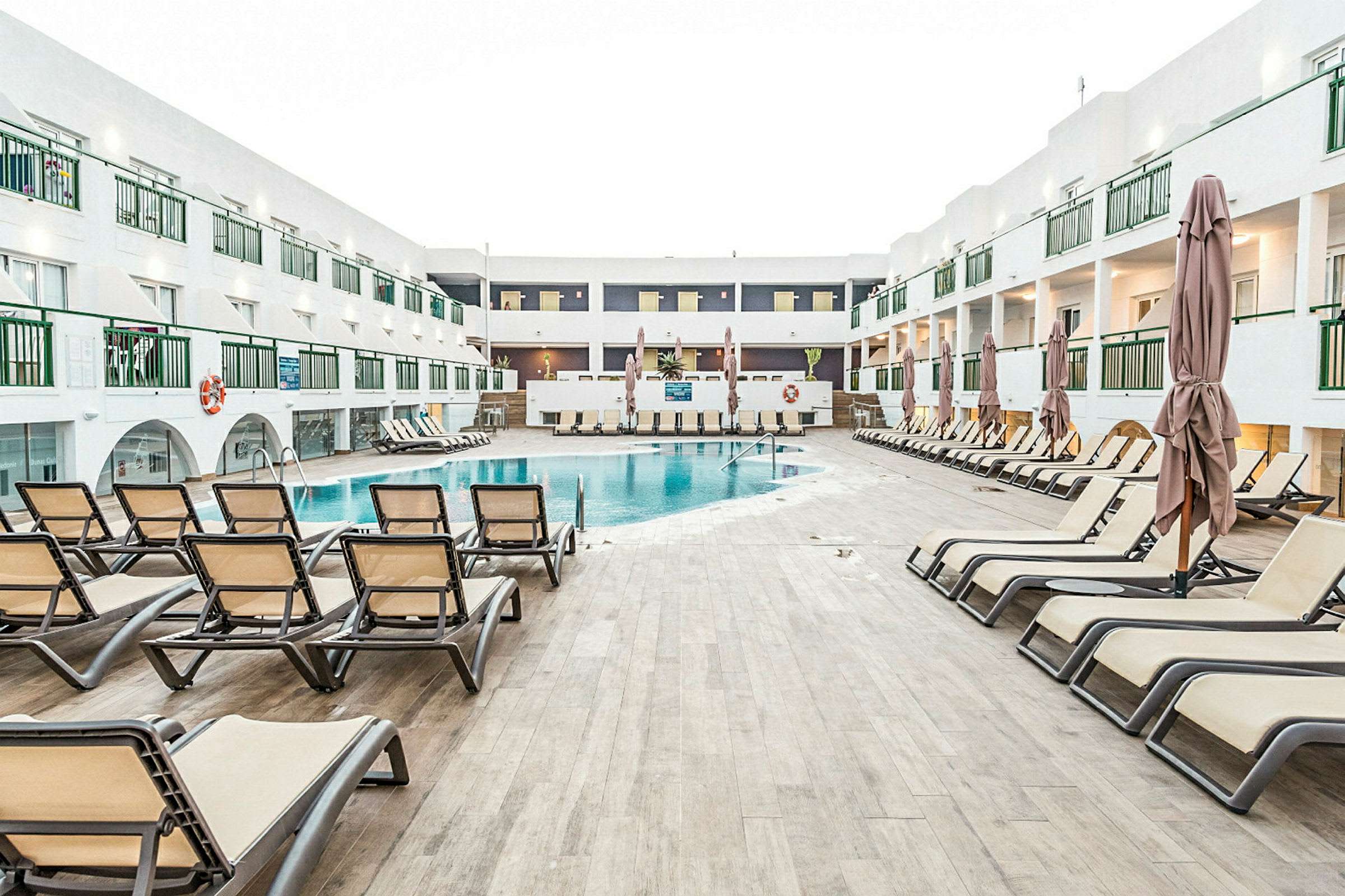Billede der viser en pool omgivet af liggestole og et hotelkompleks i baggrunden. (AI-genereret tekst)