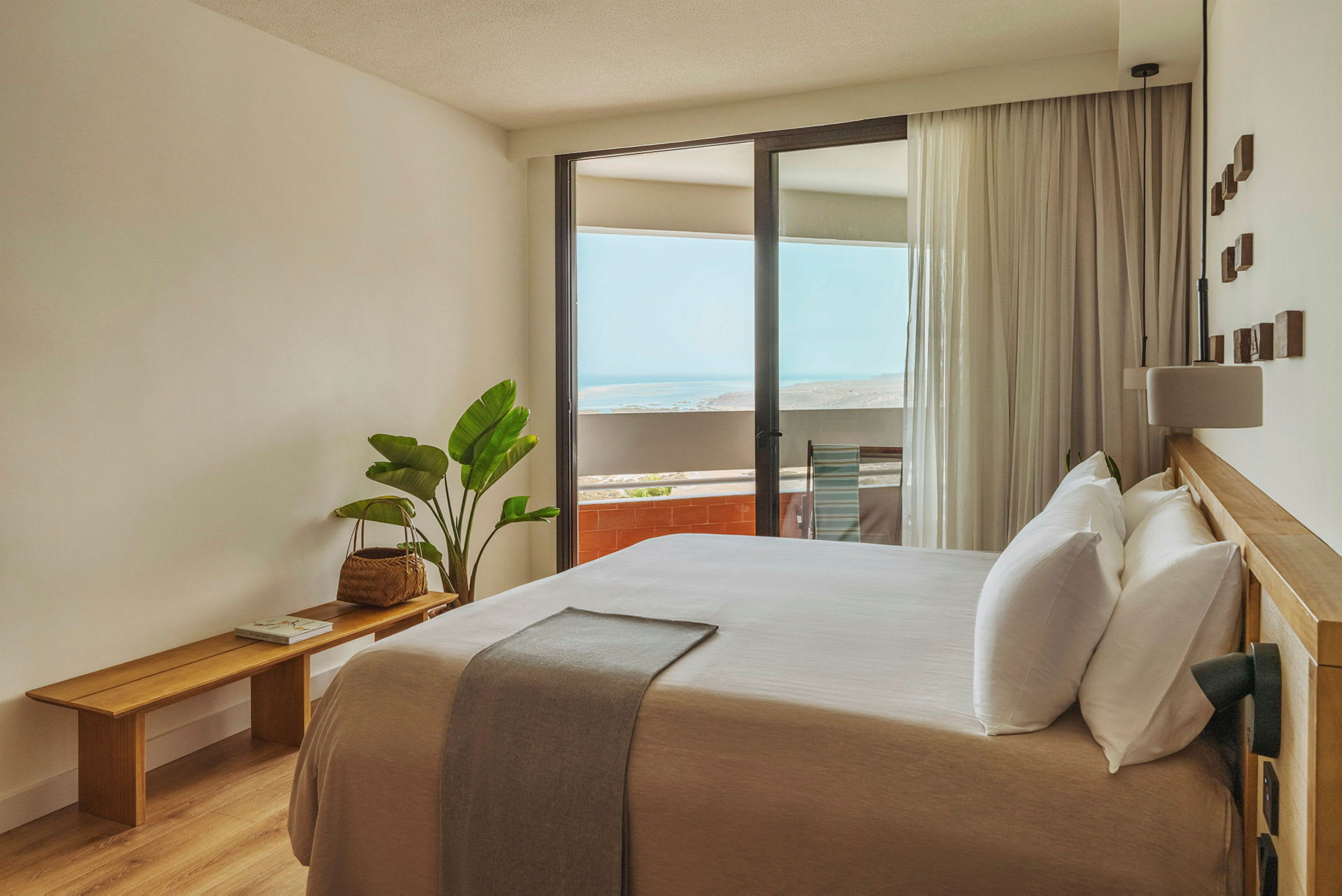 Et lyst og moderne indrettet hotelværelse med en stor seng og en balkon med udsigt over havet. (AI-genereret tekst)