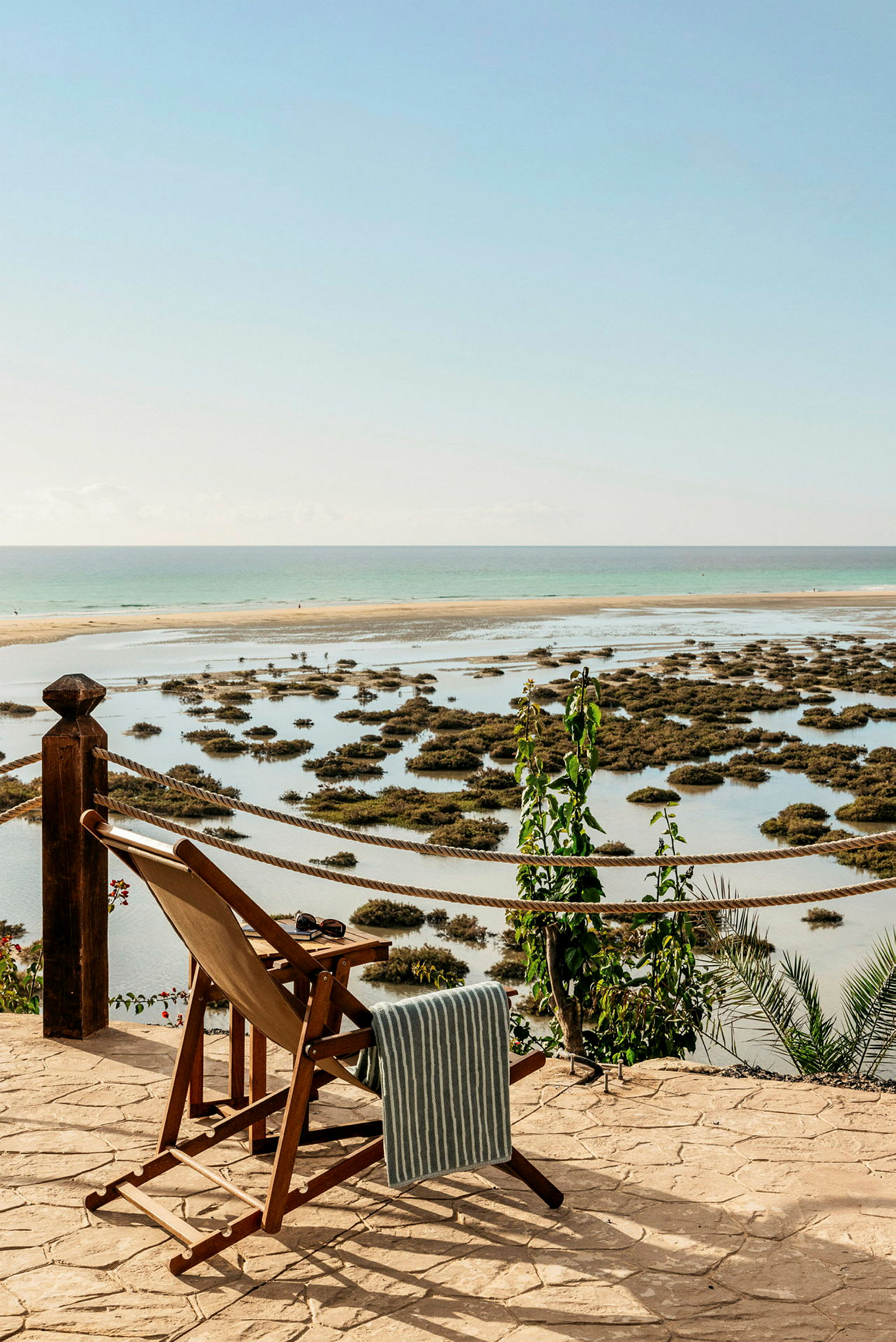 En liggestol står på en terrasse mod havet, med en frodig udsigt over vandspejle og vegetation i baggrunden. (AI-genereret tekst)