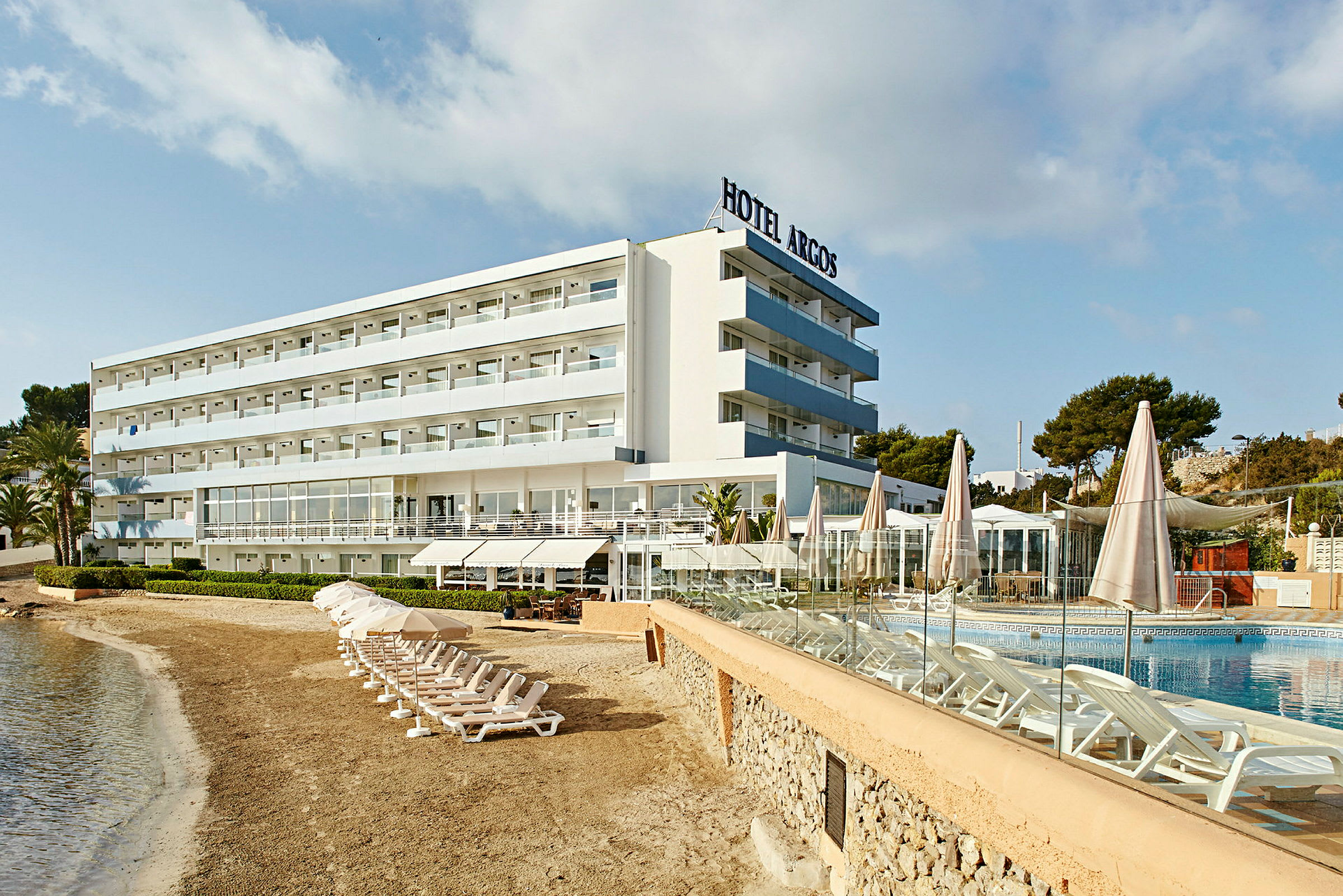Et hotel ved stranden med liggestole ved poolen. (AI-genereret tekst)