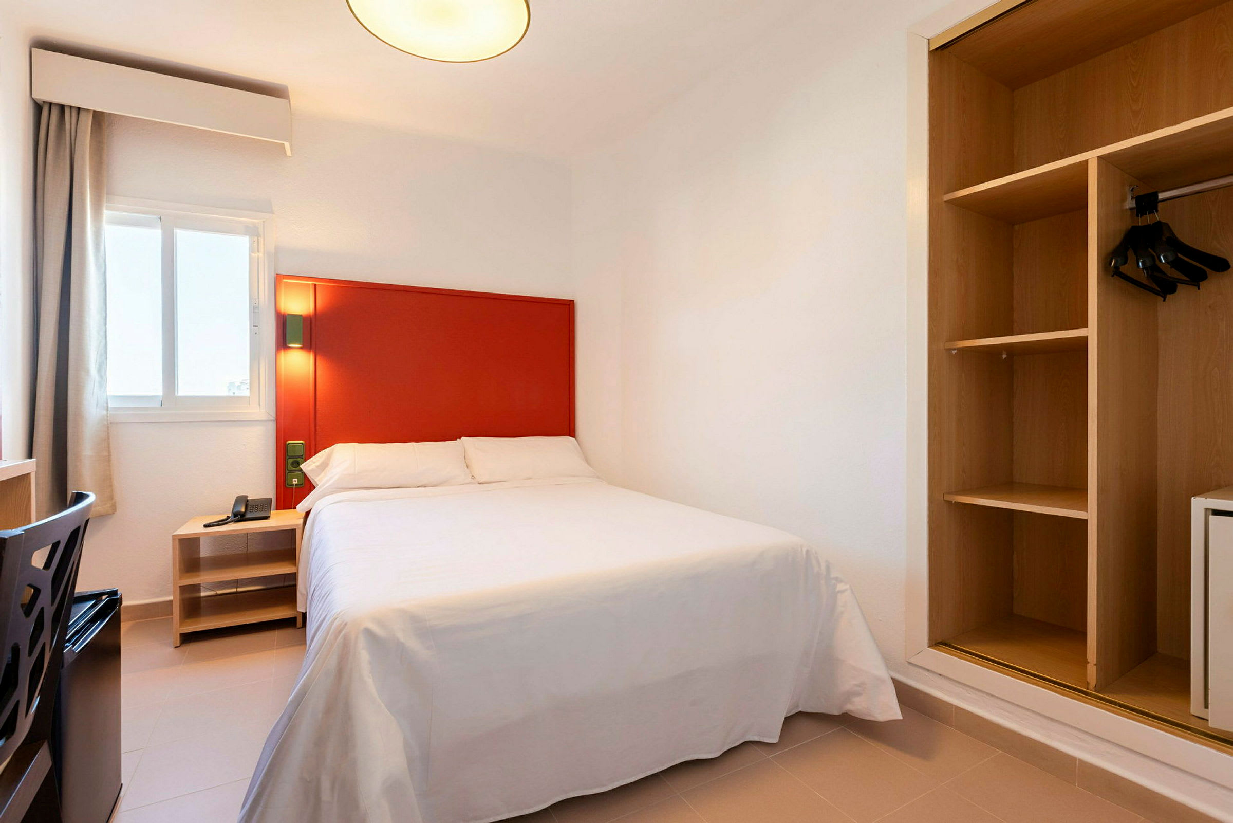 Billede af et hotelværelse med en seng, rød sengegavl og åben garderobe. (AI-genereret tekst)
