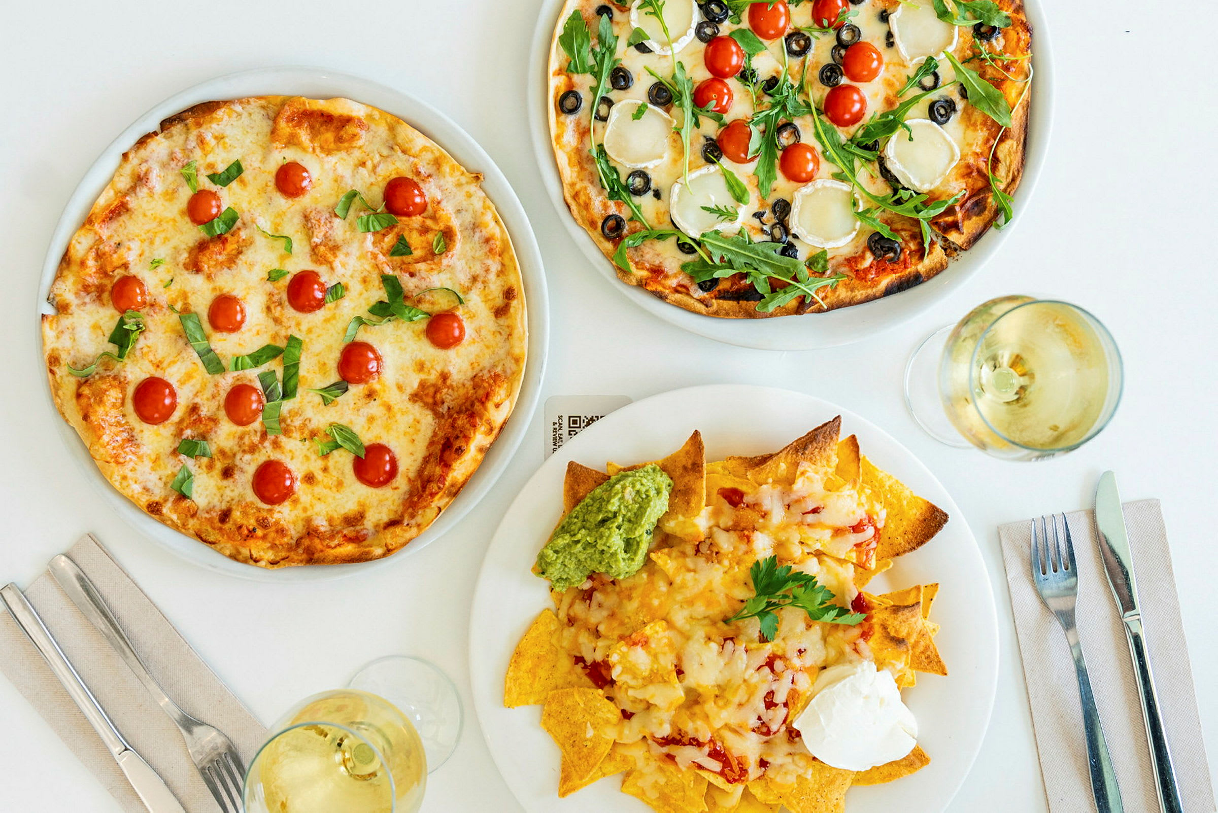 To pizzaer med forskellige toppings og en tallerken nachos med guacamole og creme fraiche. (AI-genereret tekst)