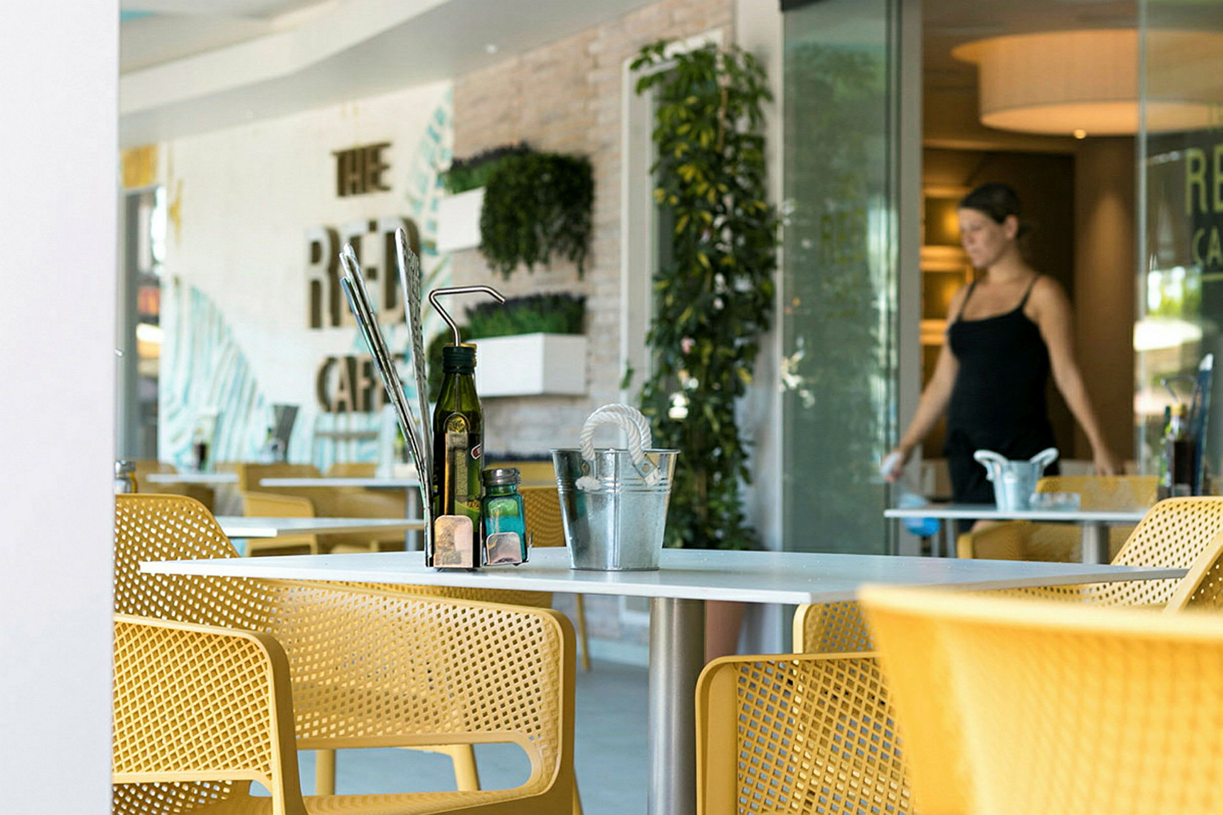 Billede af en moderne caféinteriør med gule stole og et bord med flasker og tilbehør på. (AI-genereret tekst)