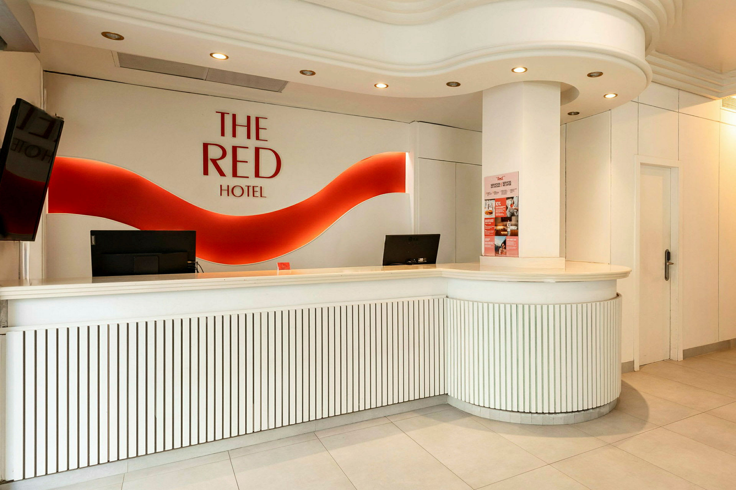 Hotelreception med hvidt interiør og rødt logo på væggen. (AI-genereret tekst)