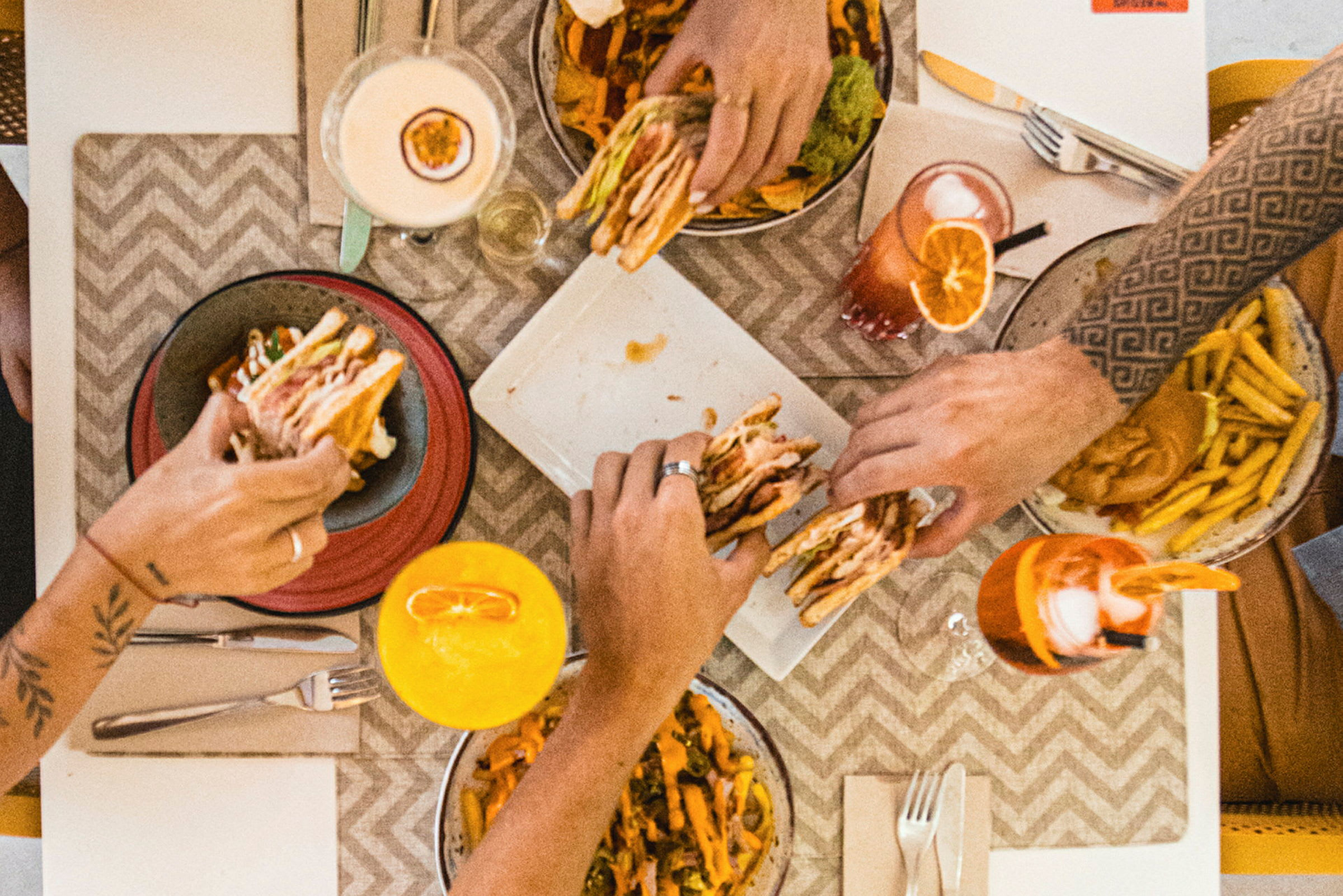 Fire personer spiser burgere, pommes frites og drikker farverige drikke ved et bord. (AI-genereret tekst)