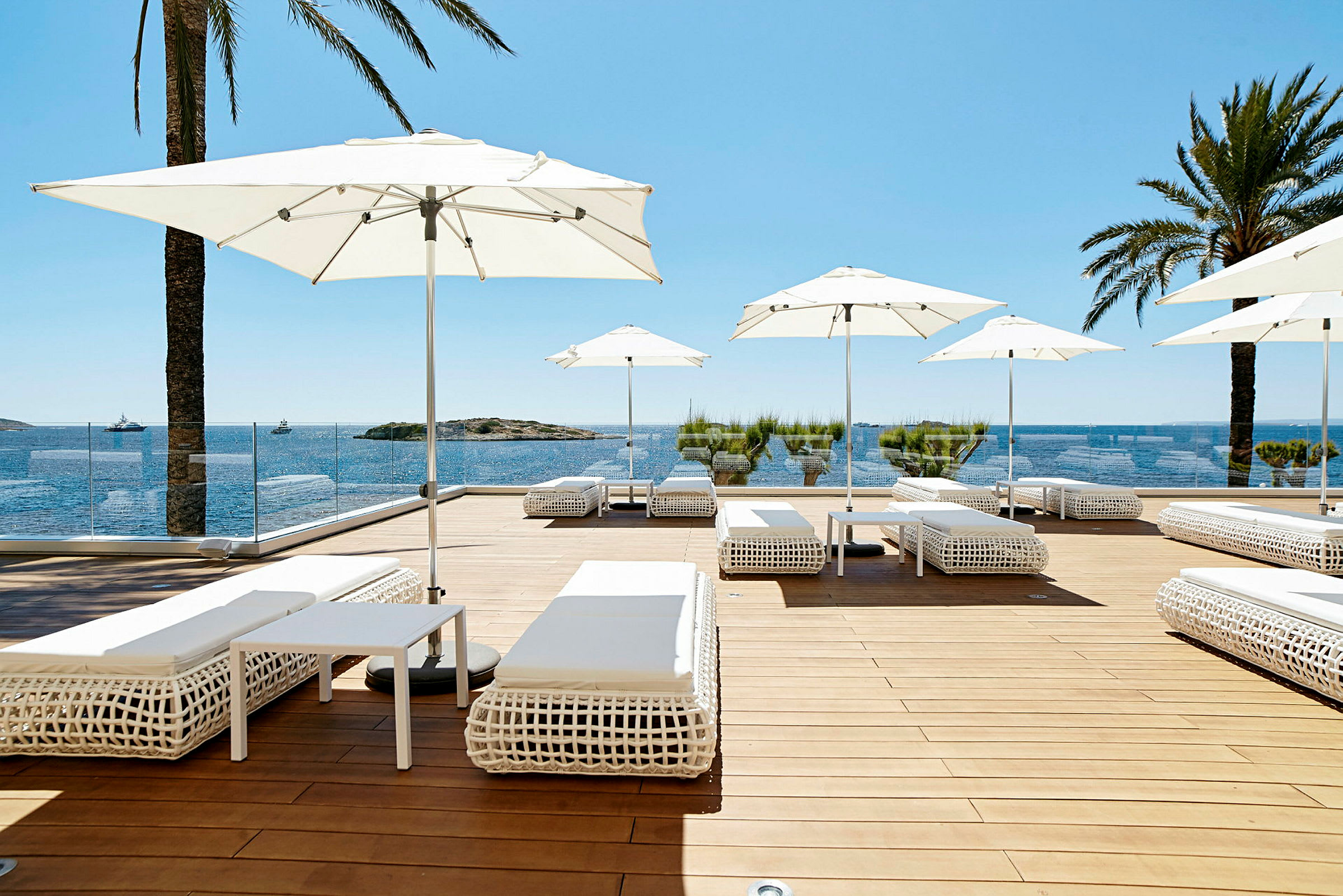 Solterrasse med hvide solsenge og parasoller, udsigt over havet og blå himmel. (AI-genereret tekst)