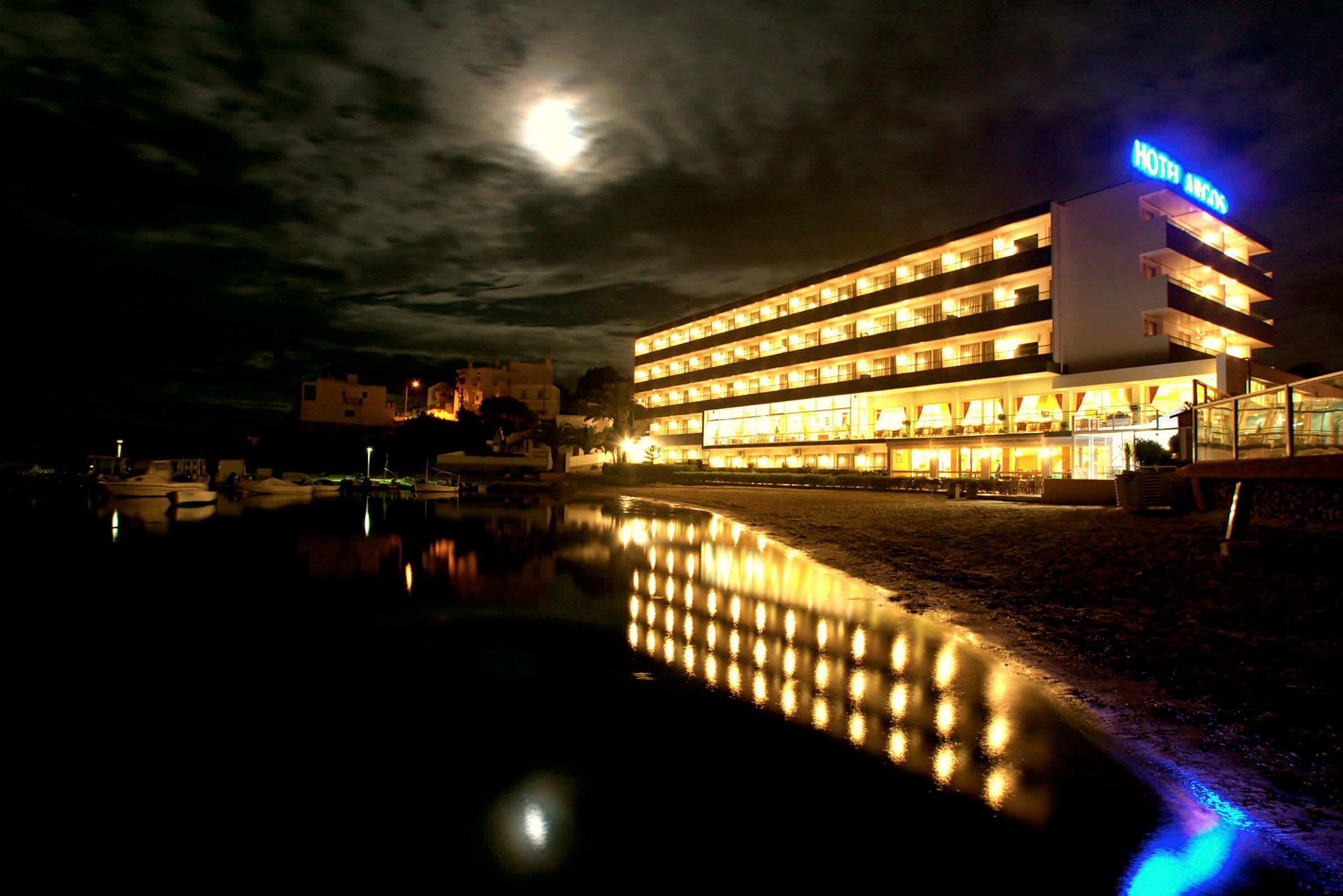Et hotel oplyst om natten med en afspejling i vandet foran. (AI-genereret tekst)