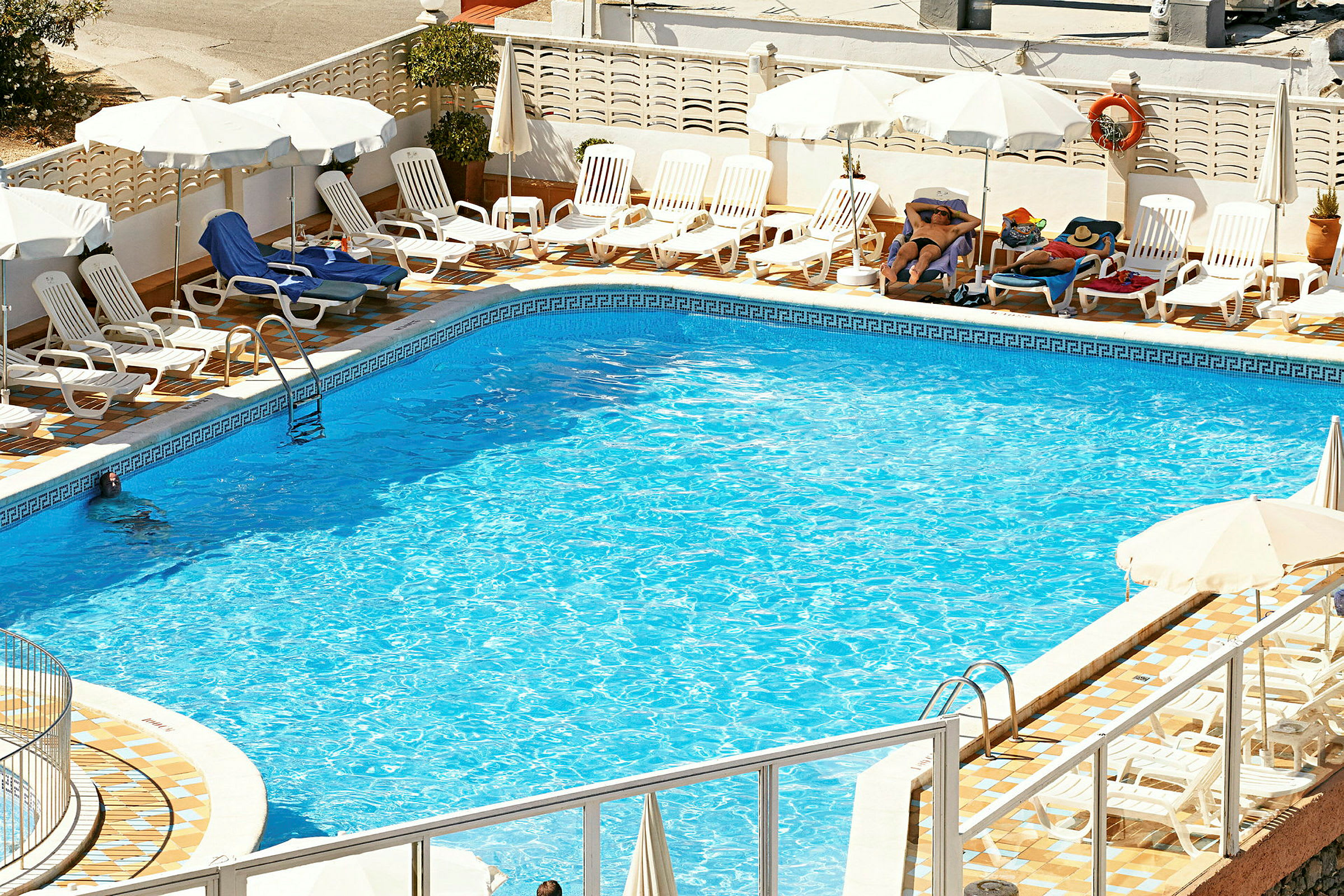 En udendørs swimmingpool omgivet af liggestole og parasoller. (AI-genereret tekst)