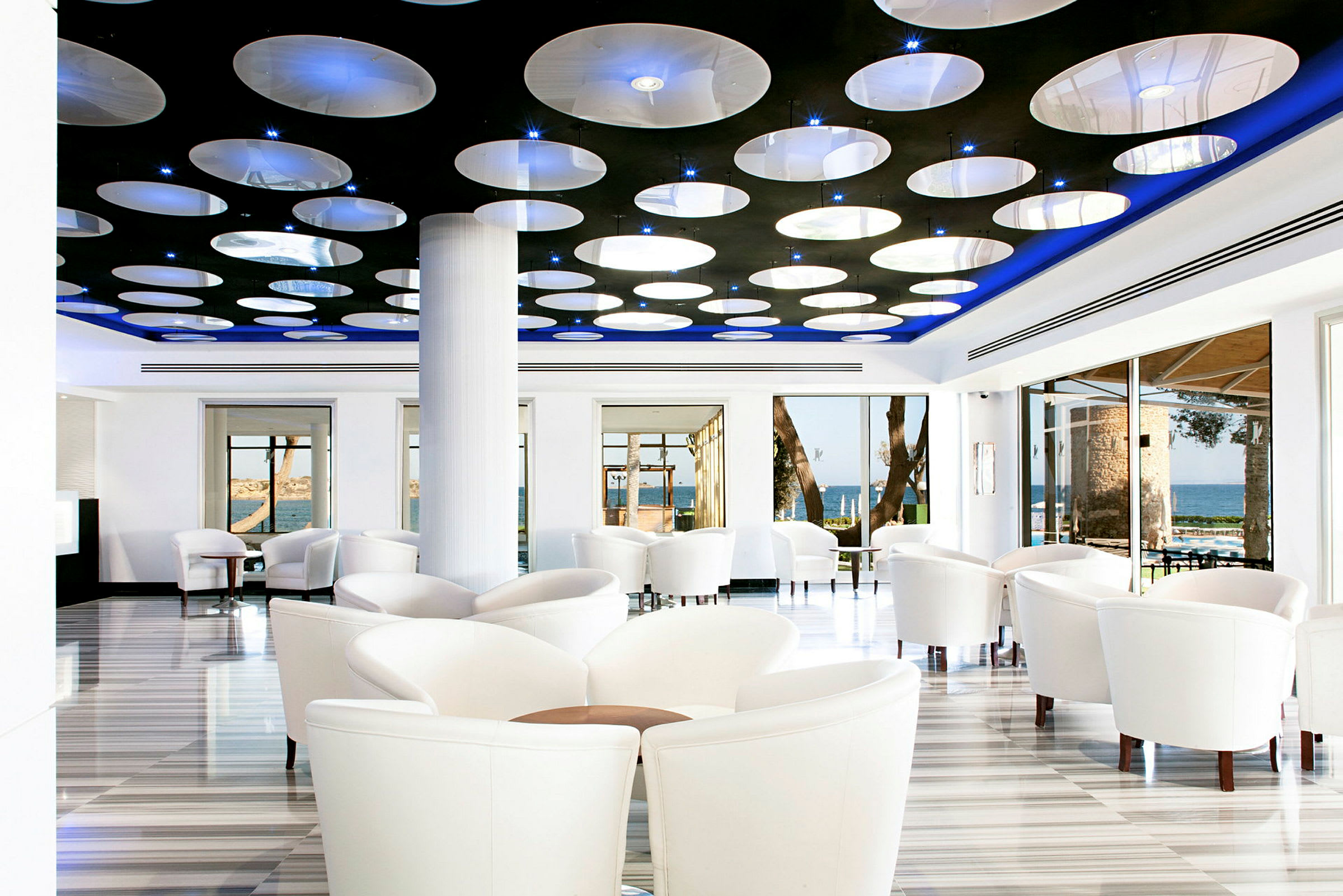 En moderne indrettet café eller lounge med hvide stole, store vinduer og et loftdesign med runde lamper. (AI-genereret tekst)