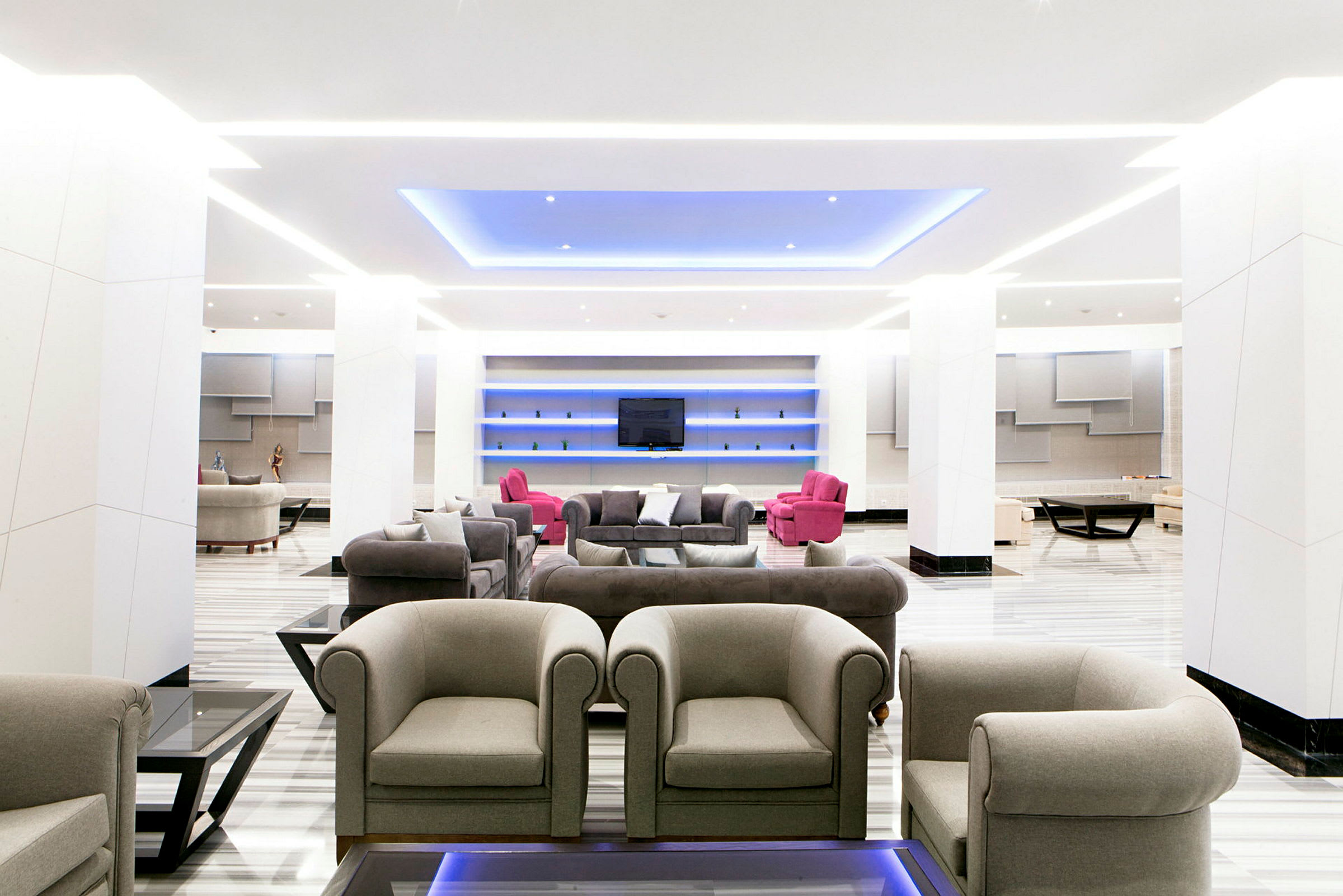 En moderne lounge med grå og lyserøde møbler samt blå loftsbelysning. (AI-genereret tekst)