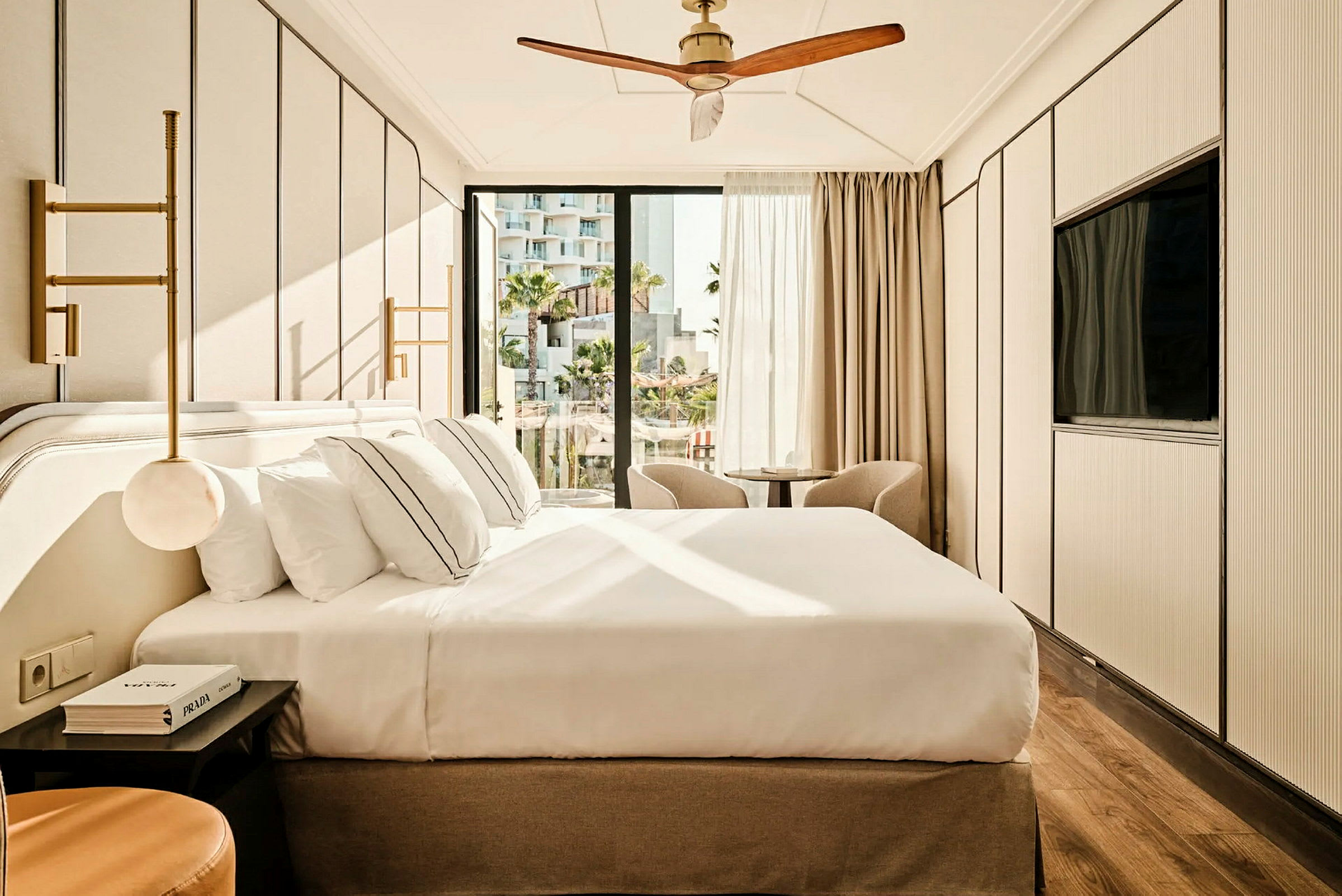 Et moderne hotelværelse med en stor seng, to stole foran vinduet og en loftsventilator. (AI-genereret tekst)