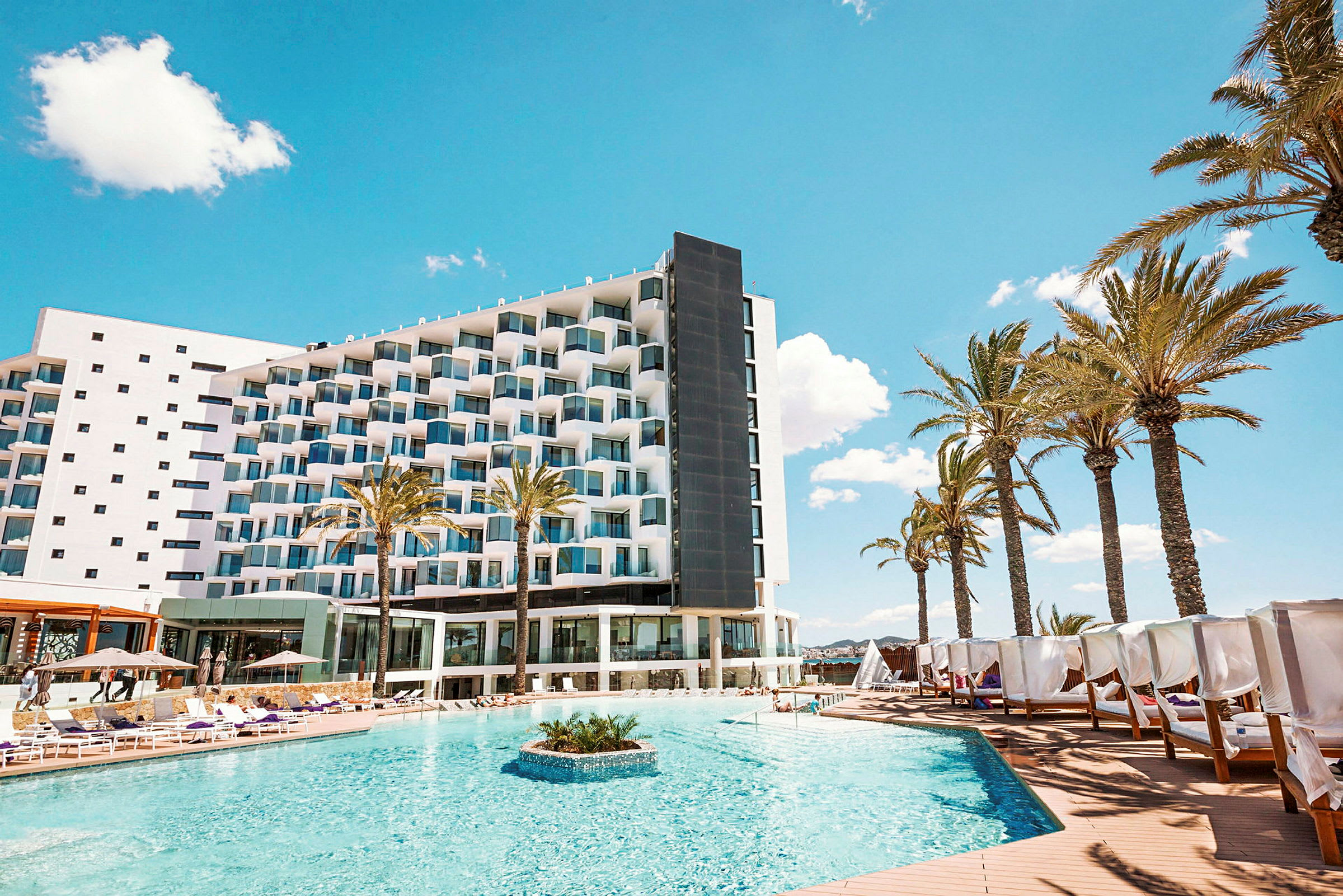 Hotel med pool og solsenge, omgivet af palmer under en blå himmel. (AI-genereret tekst)