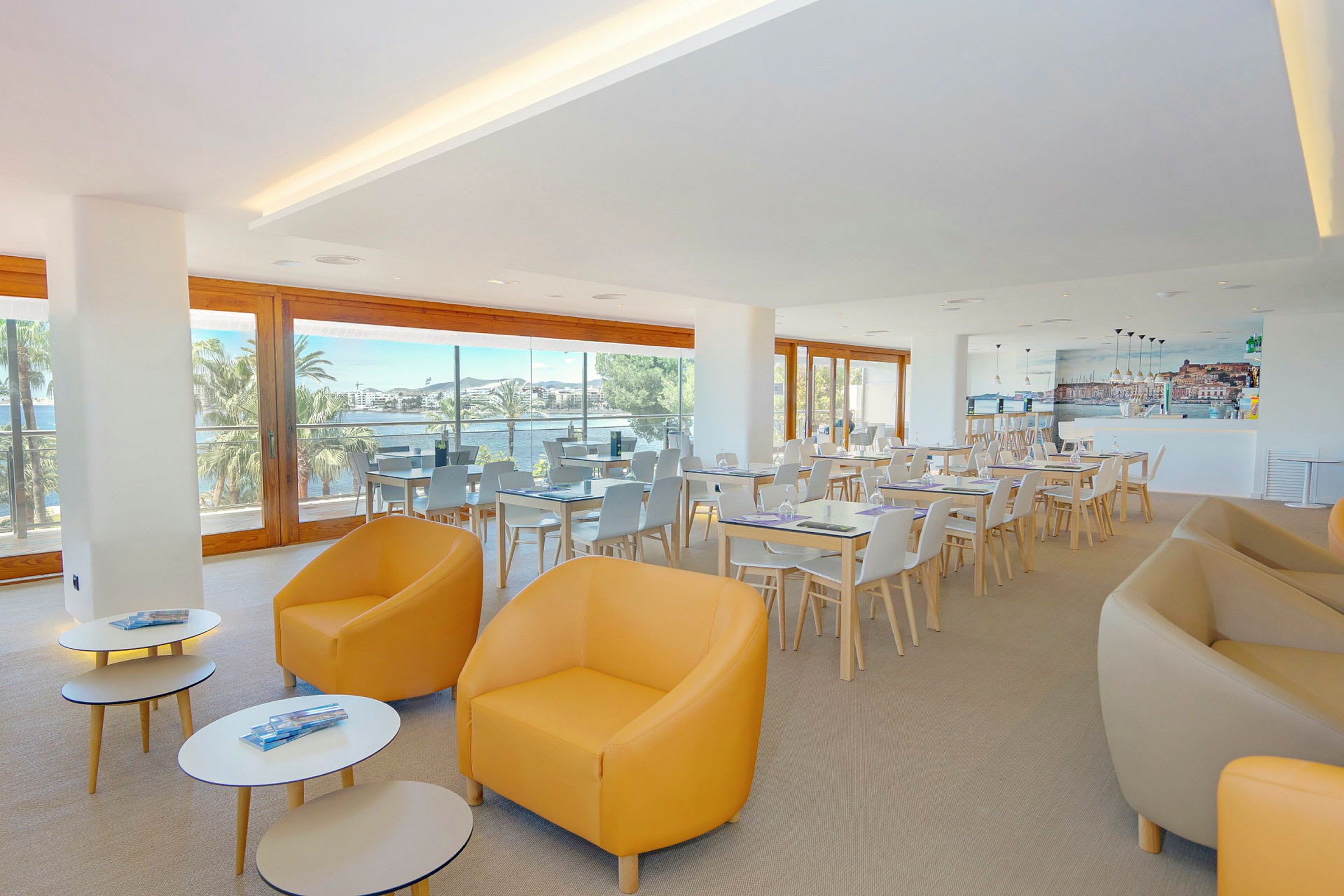 Et lyst café- eller restaurantområde med store vinduer, der lukker naturligt lys ind, siddegrupper med moderne stole og borde. (AI-genereret tekst)