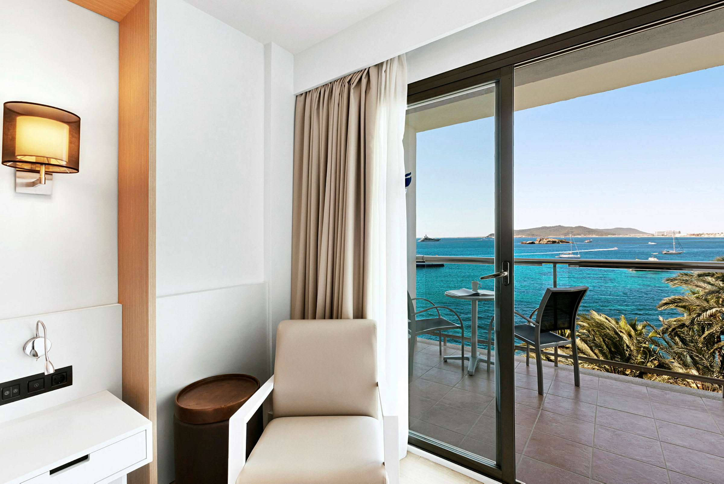 Hotelværelse med minimalistisk indretning og udsigt over havet fra en altan. (AI-genereret tekst)