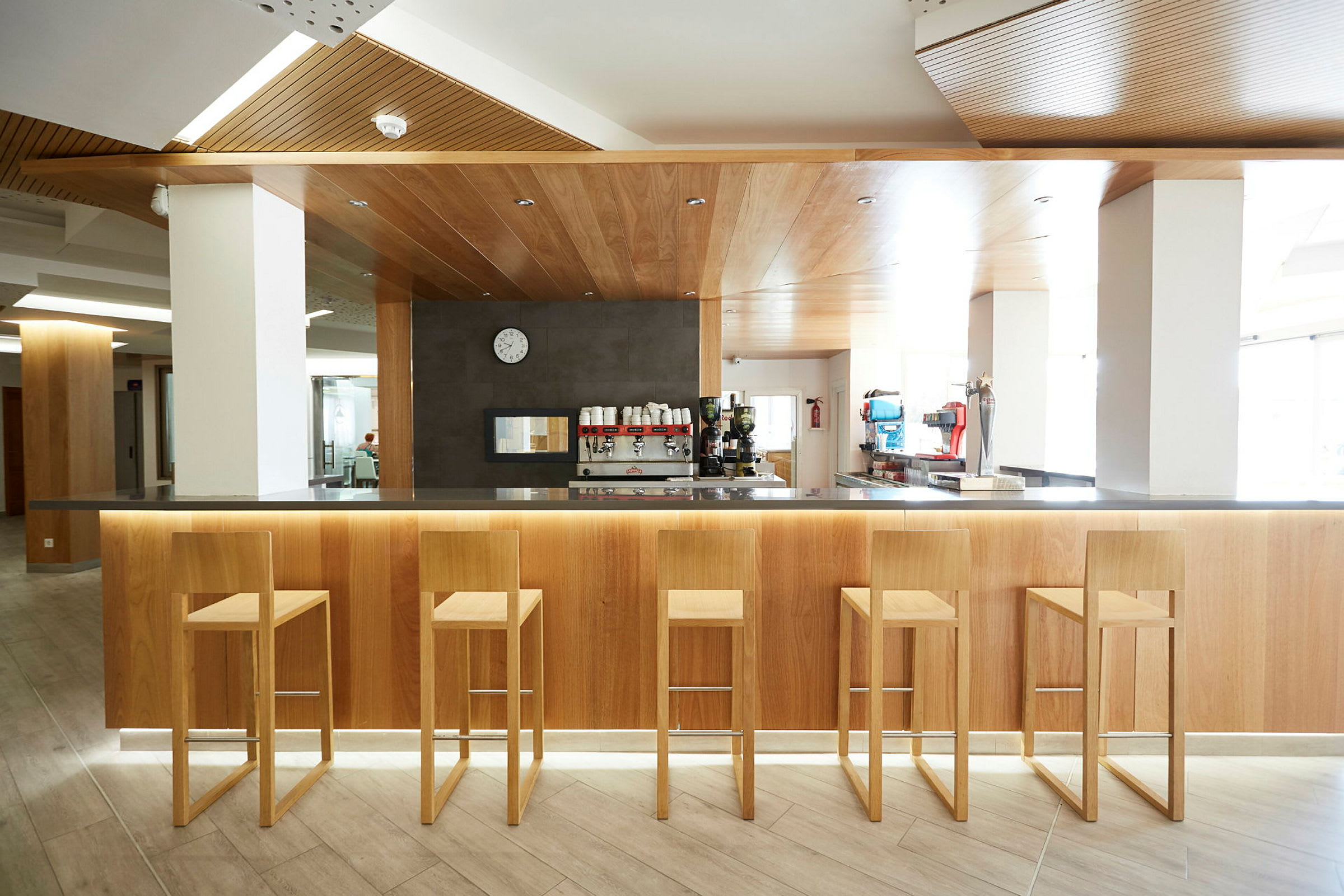 Interiørbillede af en moderne bar med fem træstole foran en bardisk af træ. (AI-genereret tekst)