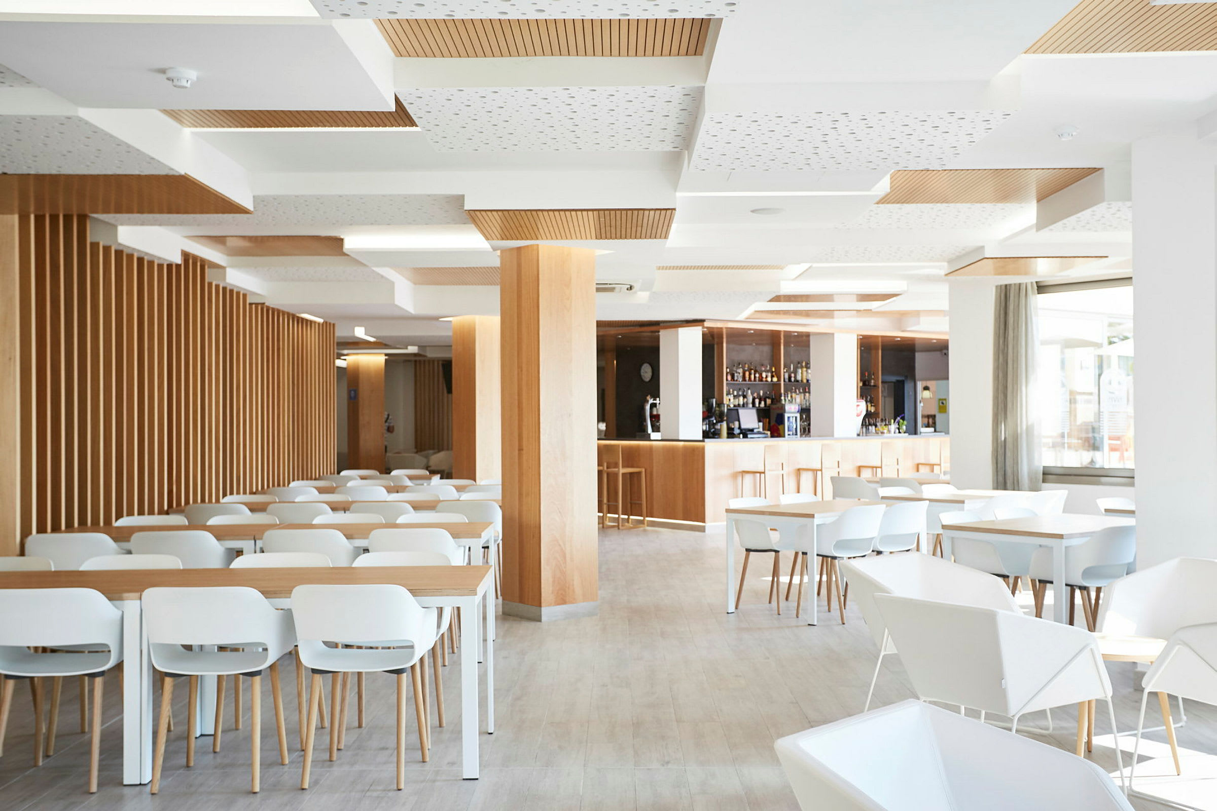 En lys og moderne restaurant med hvide stole og borde, trædetaljer og en bardisk. (AI-genereret tekst)
