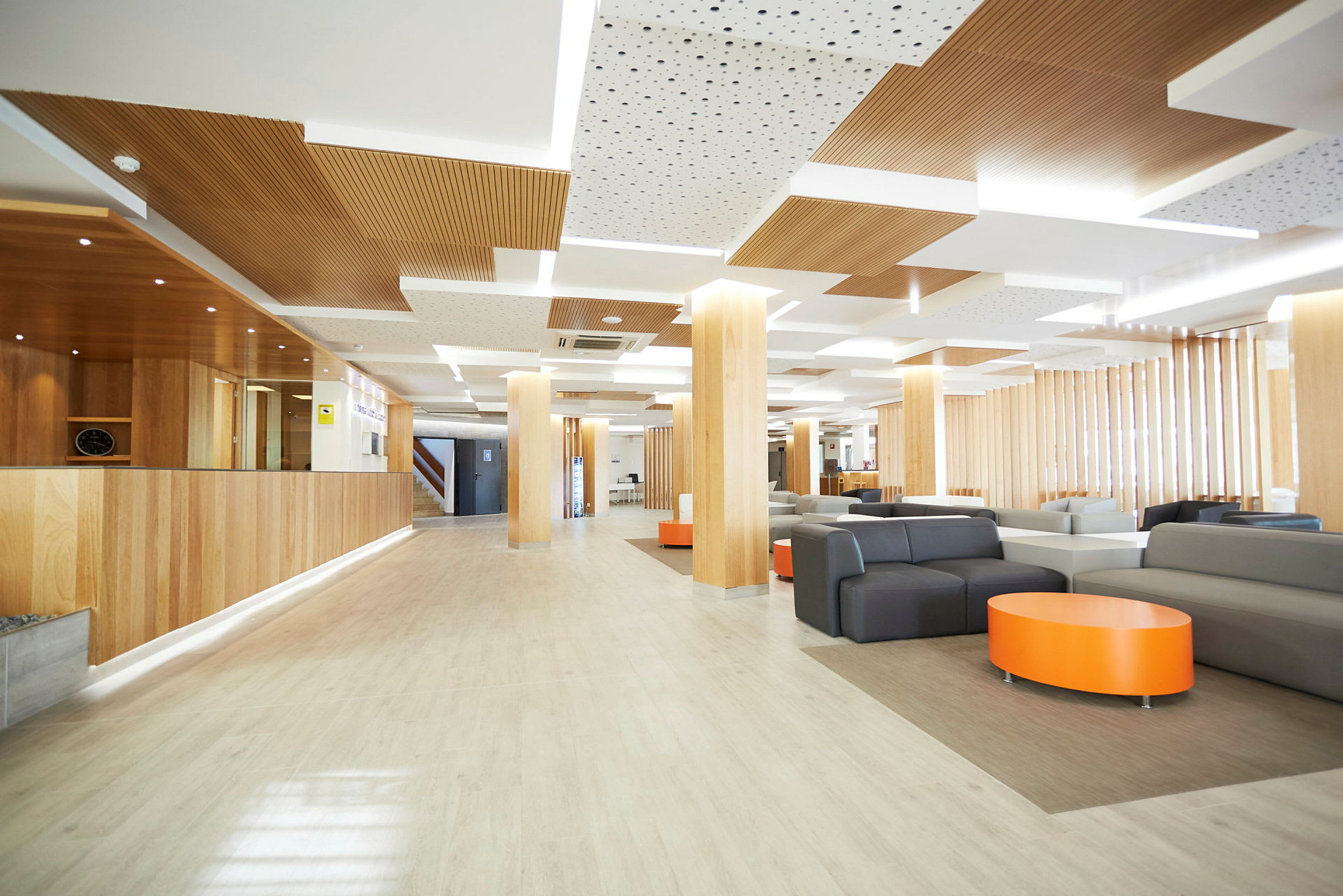 En moderne indrettet hotelreception med træpaneler, sofaer og et orange bord. (AI-genereret tekst)