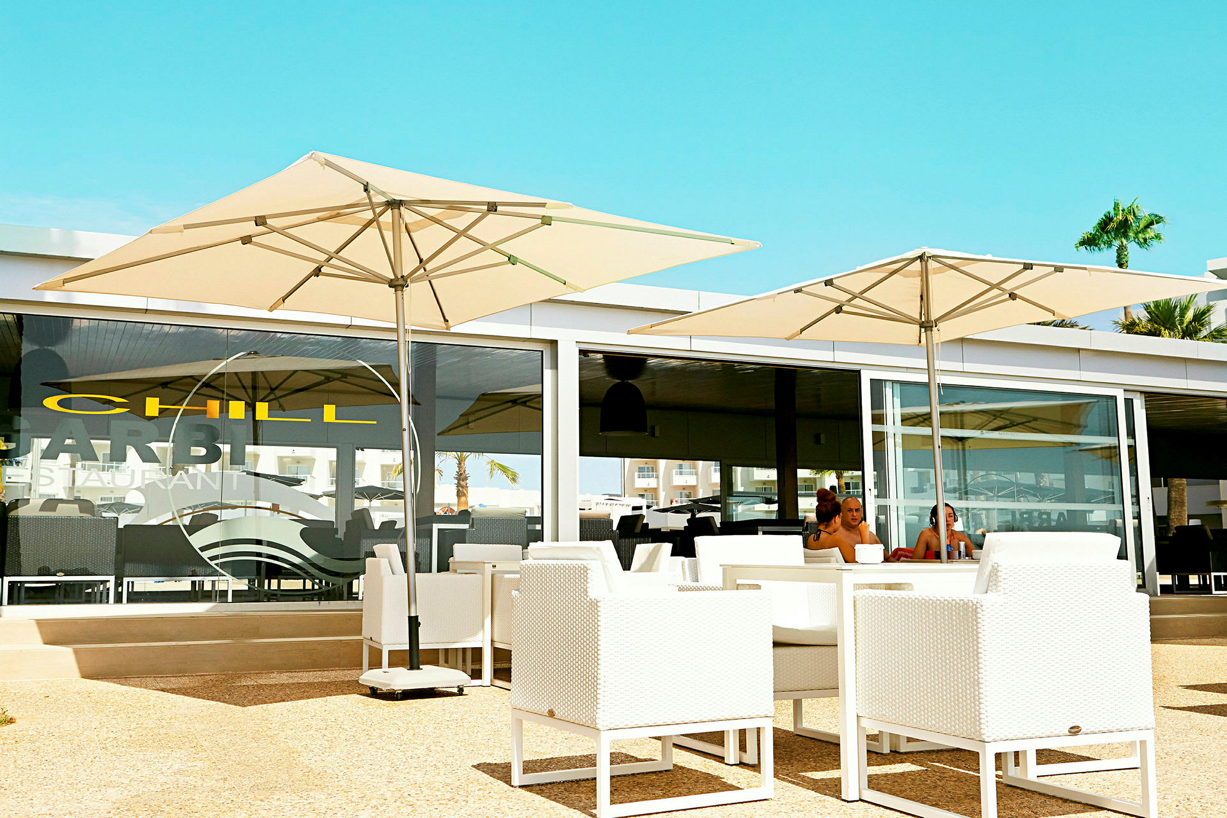 En restaurantterrasse med hvide møbler og store parasoller. (AI-genereret tekst)