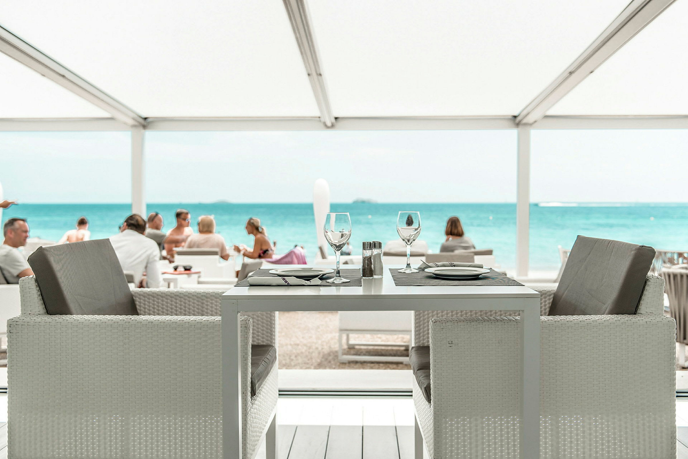Et dækket restaurantbord med udsigt over havet og en strand. (AI-genereret tekst)