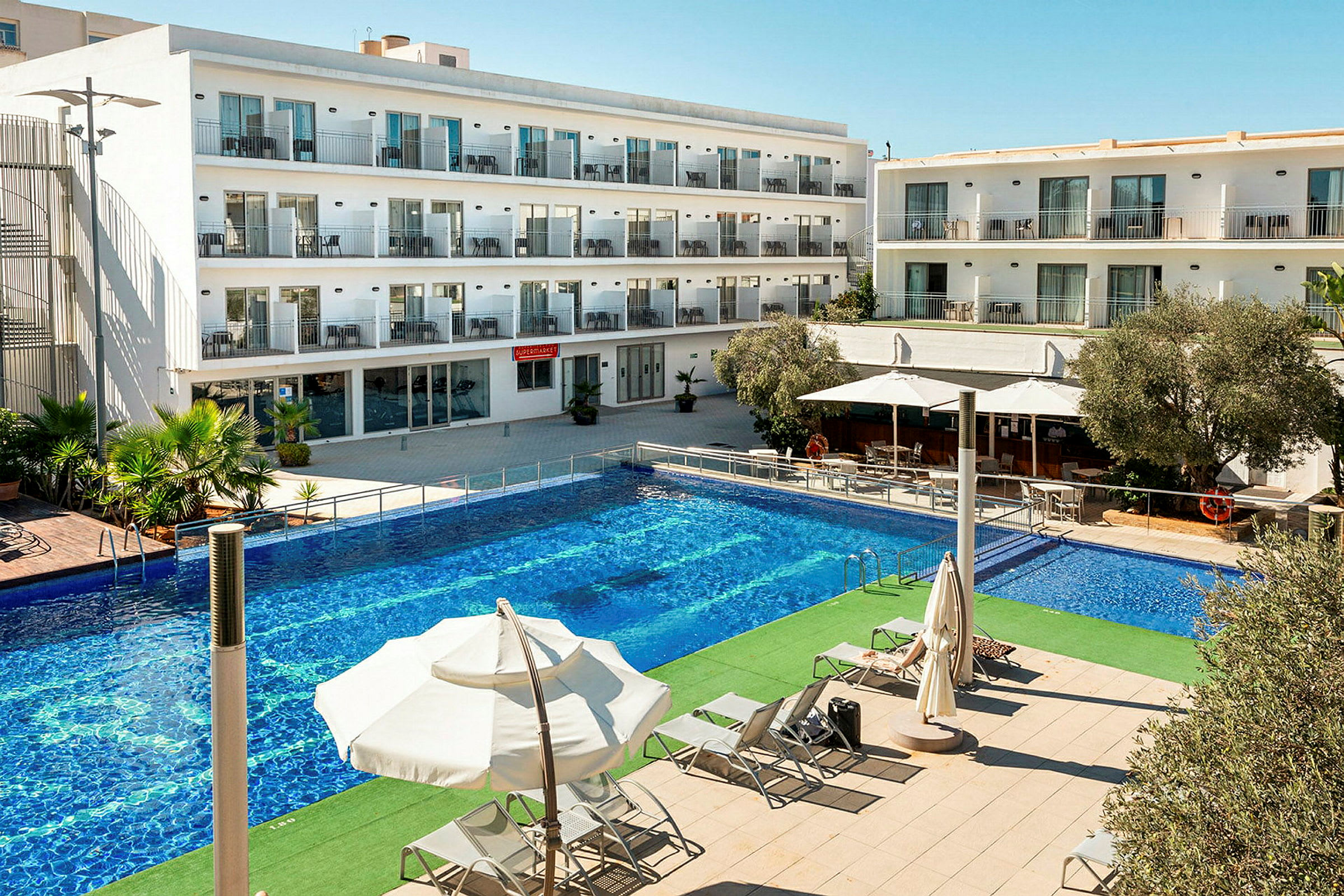 Billede af en hotelbygning med flere etager. Foran bygningen er der en stor pool og liggestole under parasoller. (AI-genereret tekst)