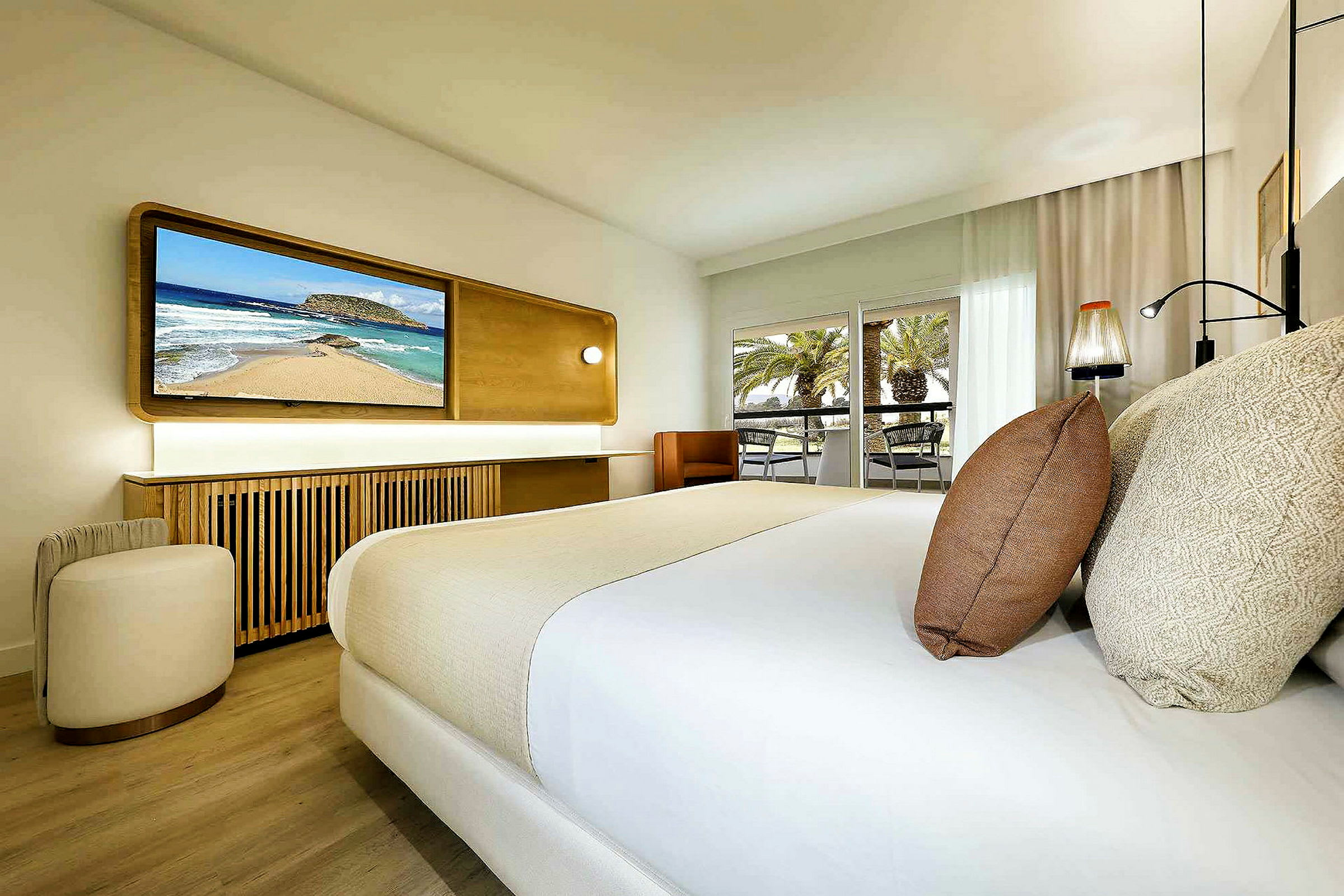 Et moderne hotelværelse med en dobbeltseng, et fjernsyn på væggen og en balkon med udsigt over palmer. (AI-genereret tekst)