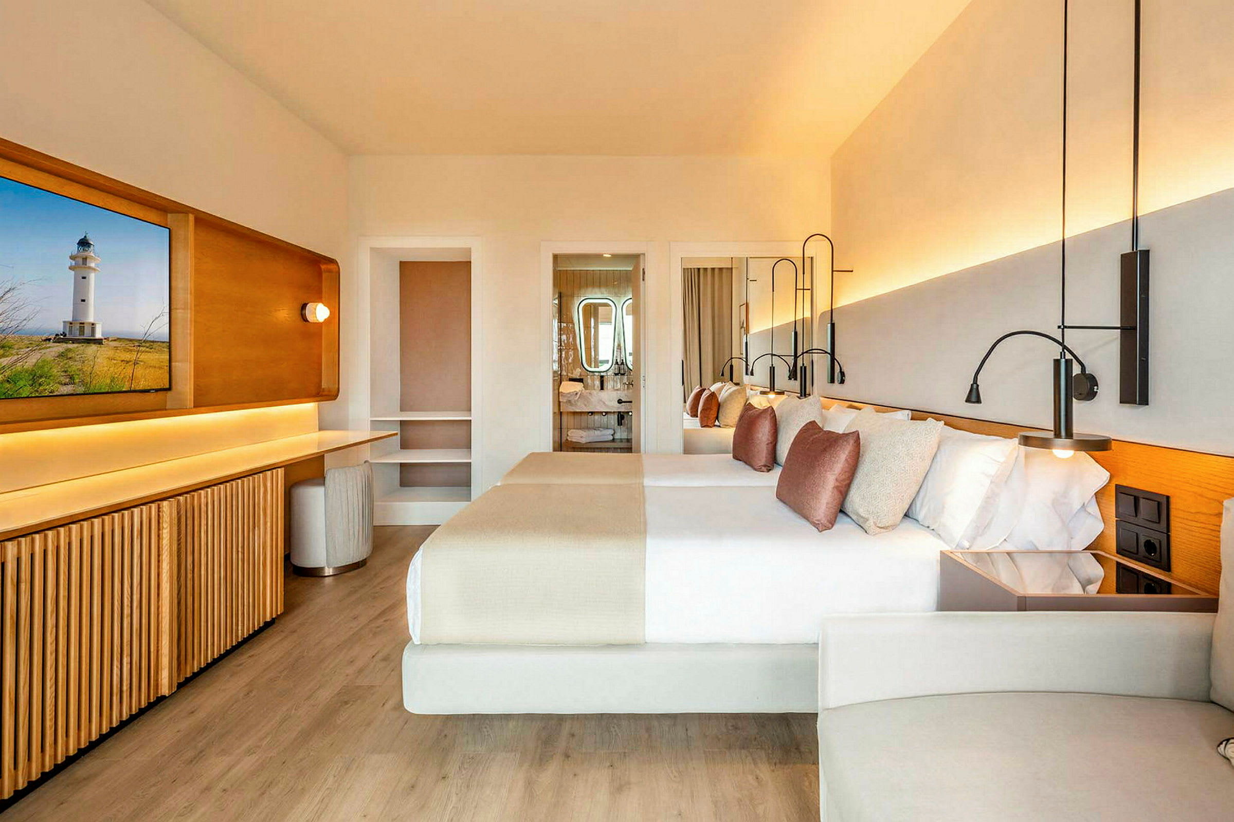 Et moderne hotelværelse med lys indretning, to dobbeltsenge med dekorative puder, et skrivebord og et badeværelse i baggrunden. (AI-genereret tekst)