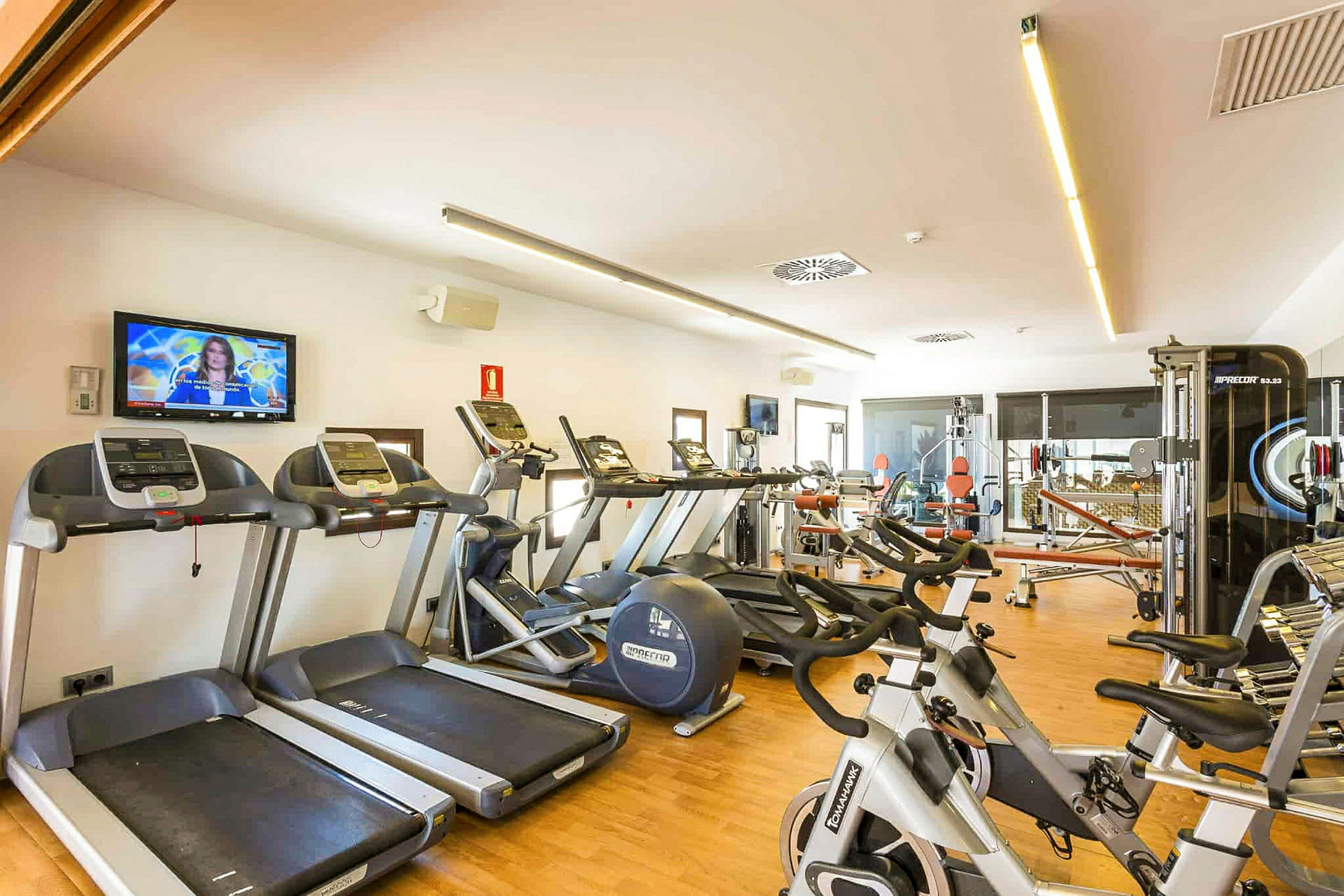 Fitnessrum med træningsmaskiner som løbebånd, motionscykler og styrketræningsudstyr. (AI-genereret tekst)