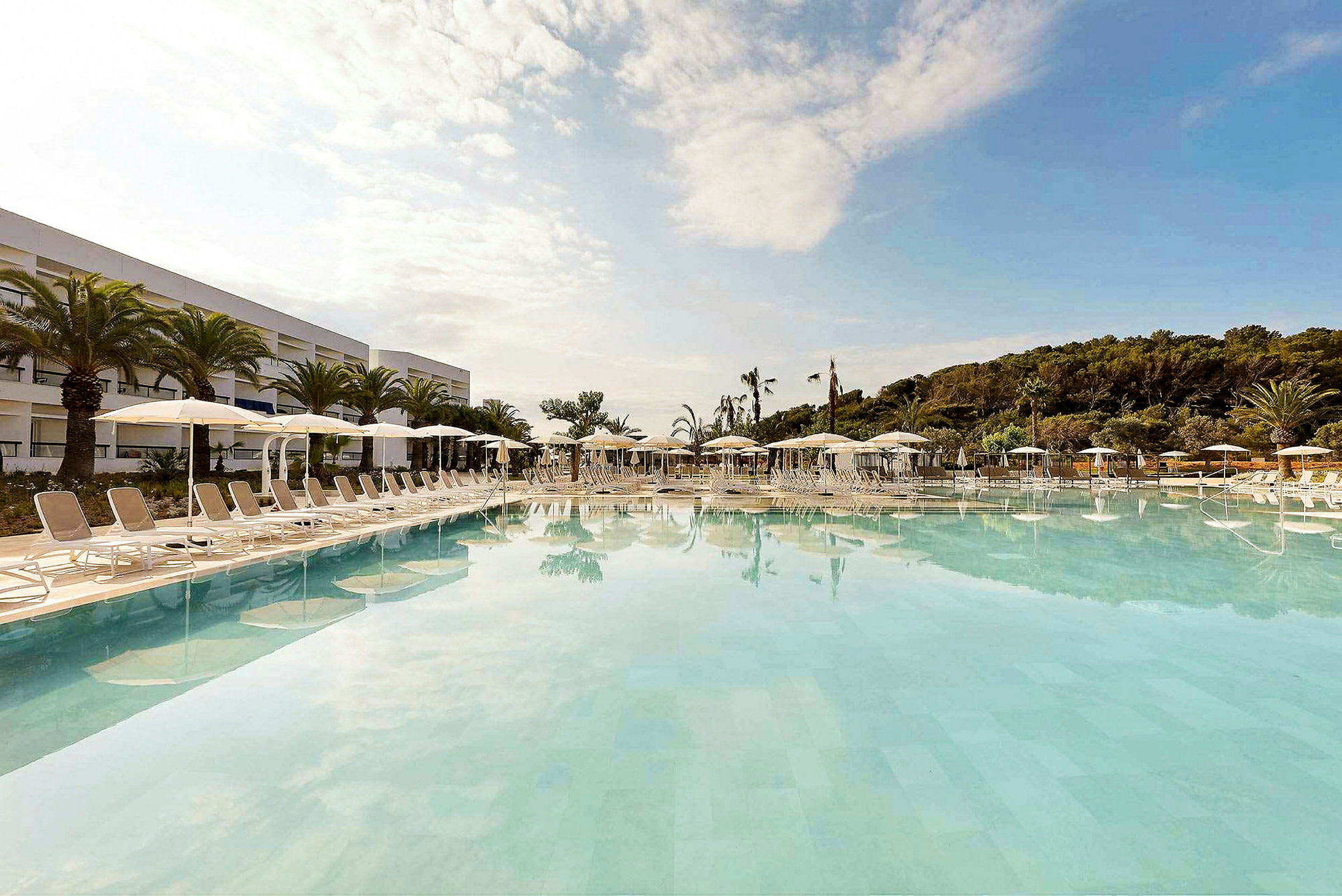 Billede af en stor pool ved et hotel, med liggestole og parasoller på den omgivende terrasse. (AI-genereret tekst)