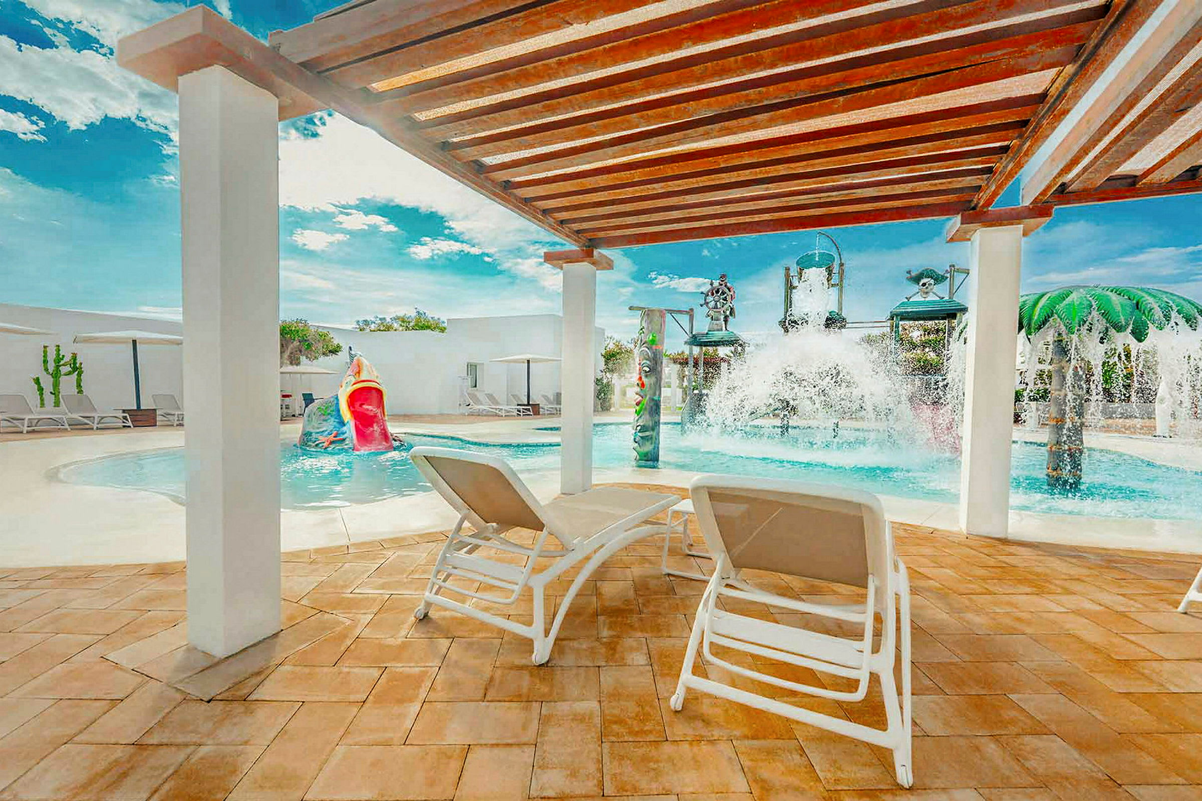 En solrig terrasse med liggestole under en pergola, tæt på en swimmingpool med vandattraktioner. (AI-genereret tekst)