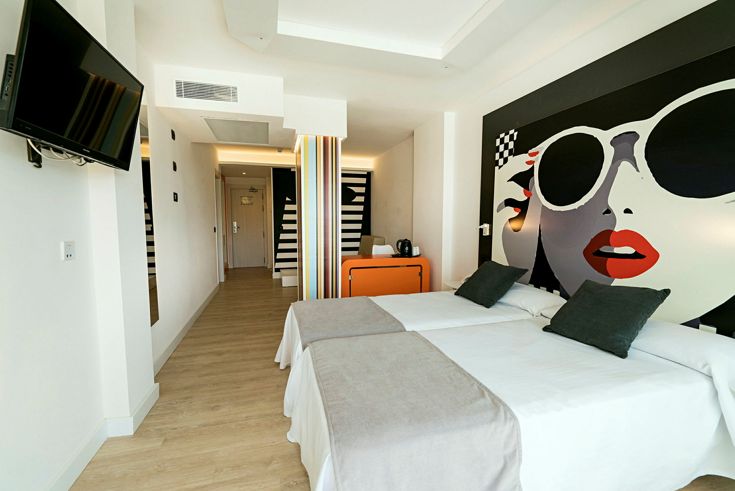 Hotelværelse med to enkeltsenge, et orange skrivebord og et vægmonteret fjernsyn. (AI-genereret tekst)