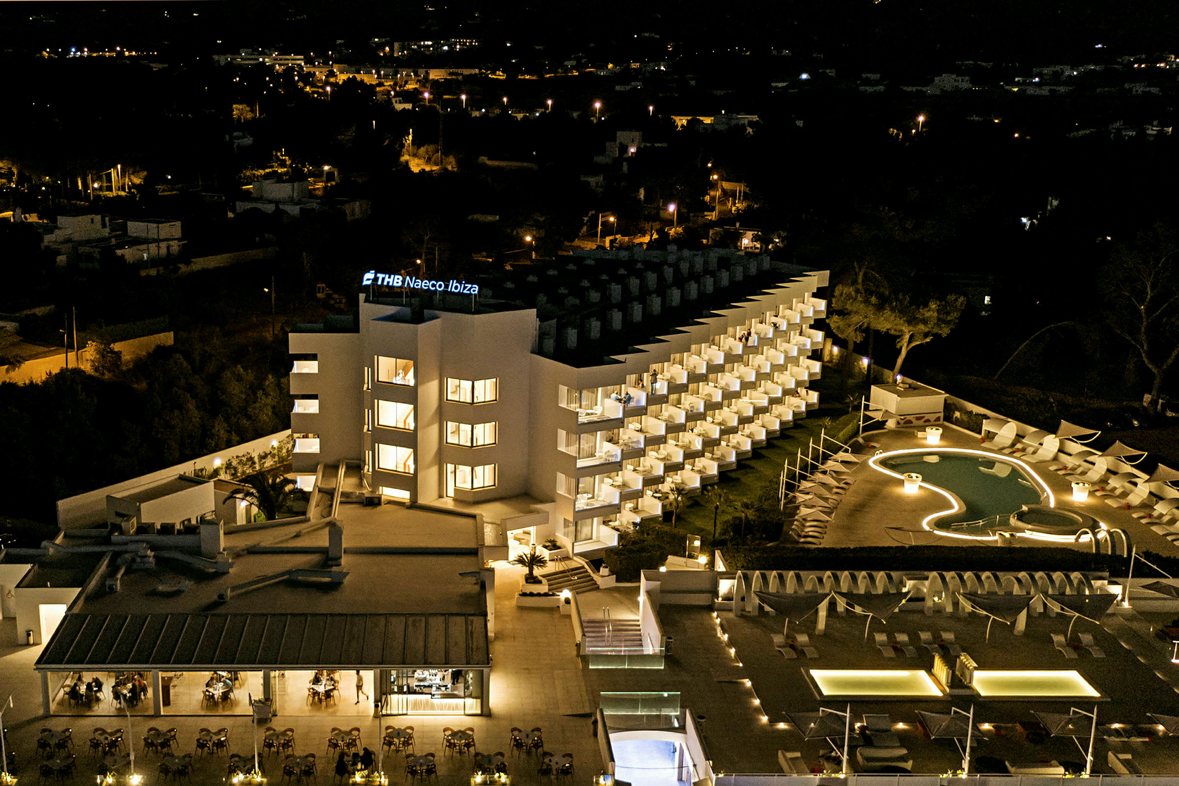 Et moderne hotel oplyst om natten med en pool foran. (AI-genereret tekst)