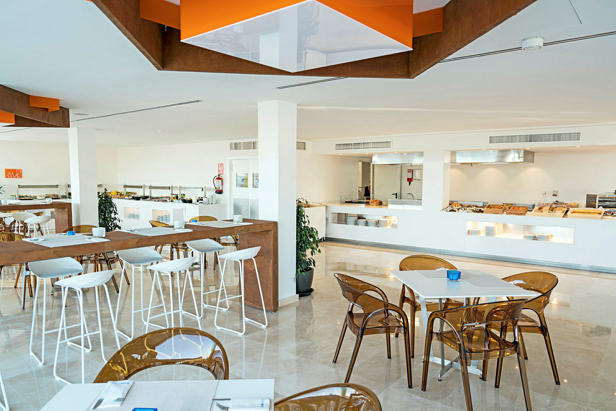 En moderne restaurant med hvide borde og stole. En buffetsektion ses i baggrunden. (AI-genereret tekst)