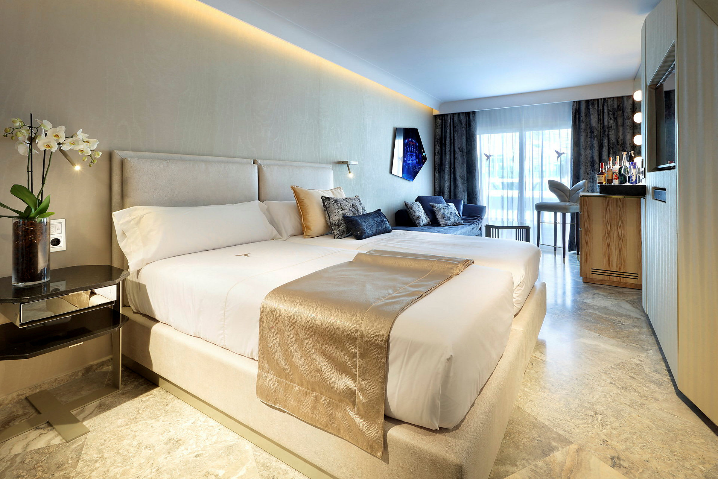 Et moderne hotelværelse med en stor seng, sofagruppe og en minibar foran et stort vindue. (AI-genereret tekst)