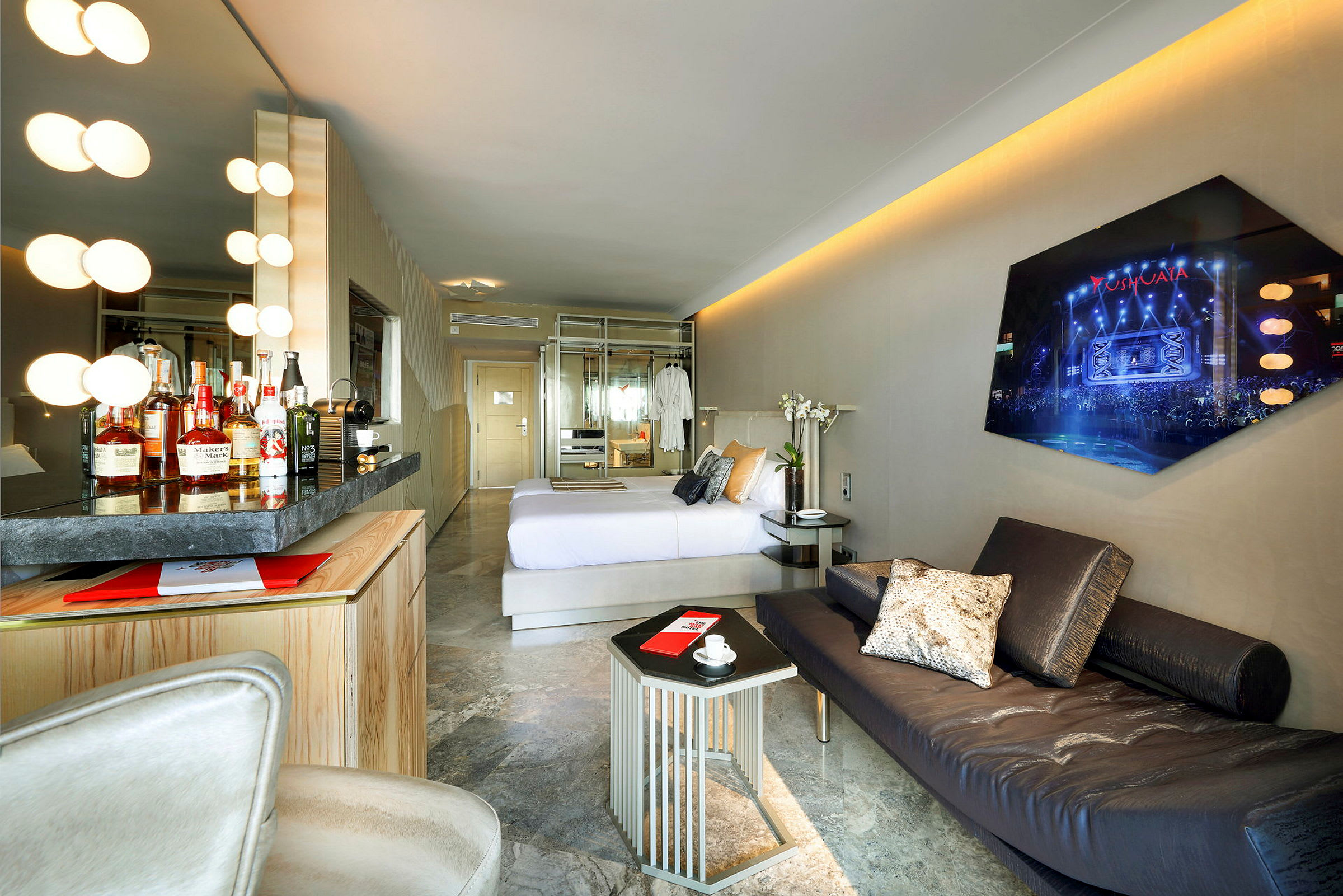 Billede af et hotelværelse med moderne design, herunder en komfortabel seng, minibar, sofa og væg-TV. (AI-genereret tekst)