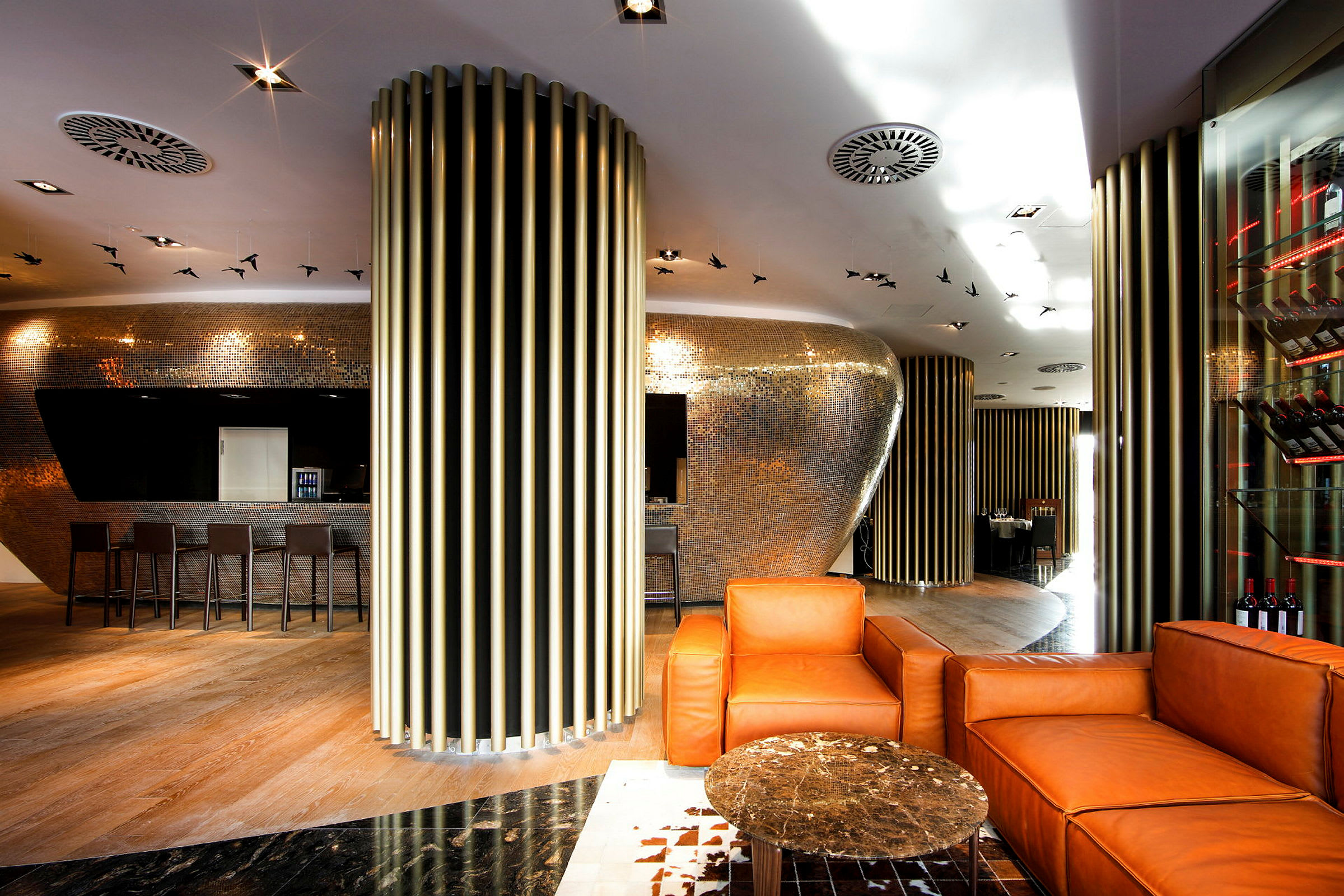Moderne indrettet lounge med orange lænestole, et lille bord og metaldekorationer på vægge og loft. (AI-genereret tekst)